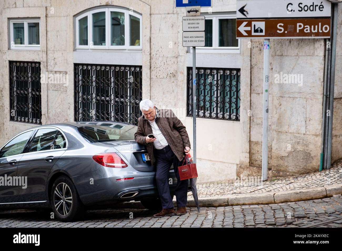 Un vieil homme âgé sur son téléphone portable avec des magasins et un parapluie, détails de la rue de Lisbonne, Portugal, mars 2022. Crédit photo : Rob Watkins Banque D'Images