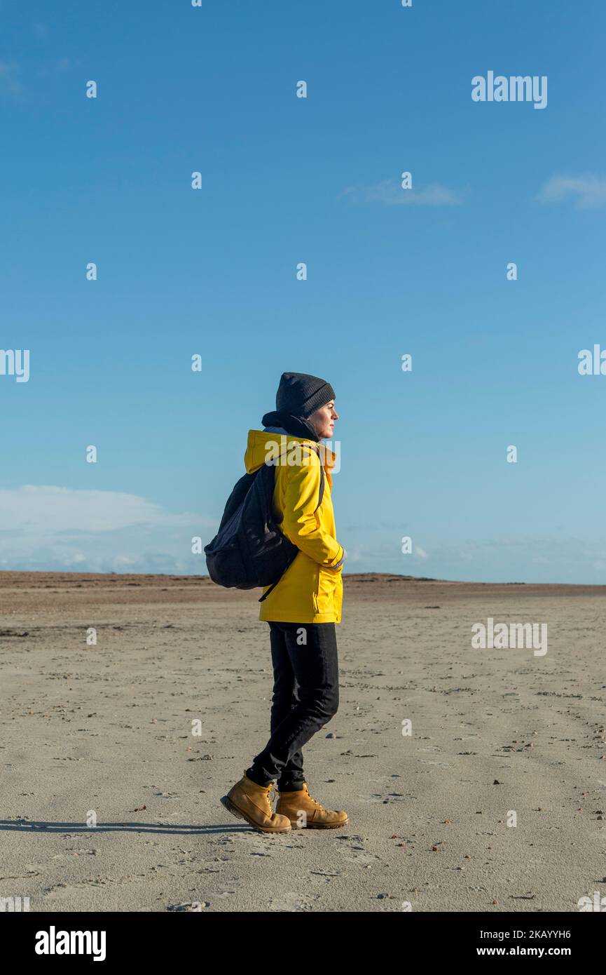 Femme portant un manteau jaune et un sac à dos marchant le long d'une plage, Sunny automne jour. Banque D'Images