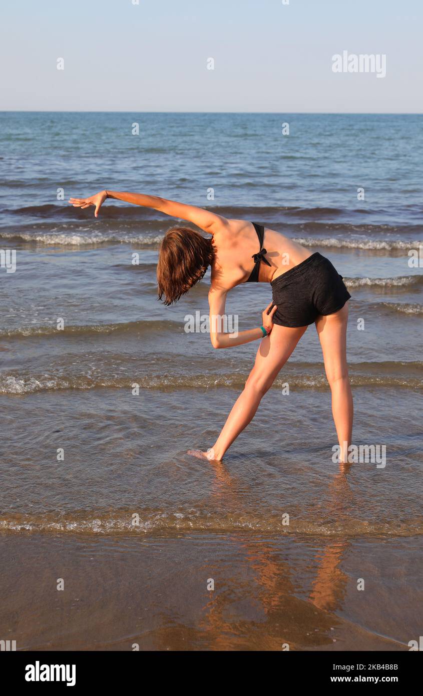 jeune fille avec maillot de bain noir effectuant des exercices de gymnastique sur la plage Banque D'Images