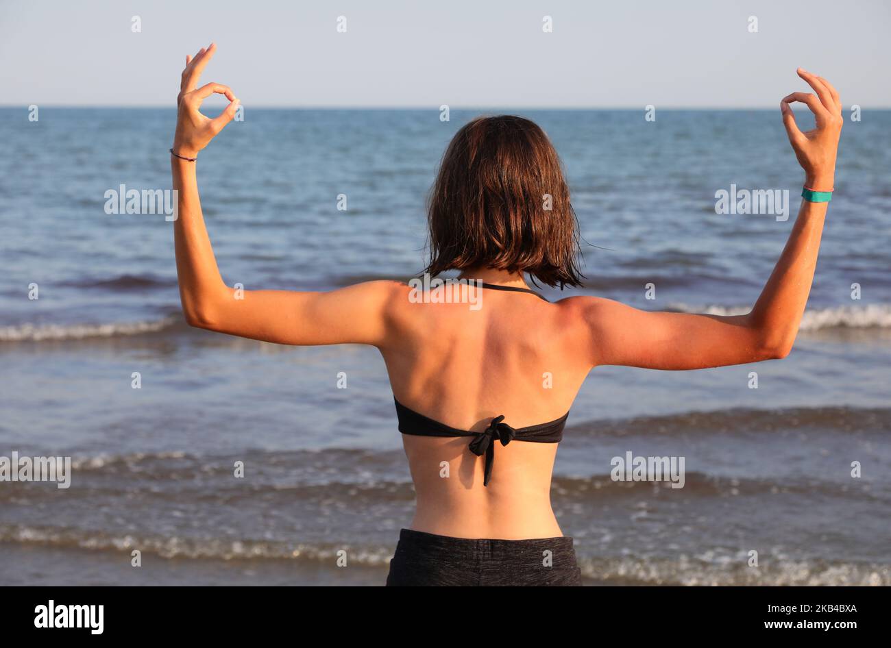 Jeune fille du dos avec la musculature développée fait OM YOGA signe au bord de la mer Banque D'Images