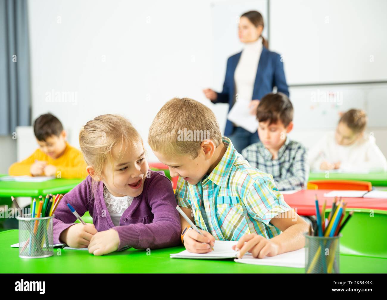 Les élèves heureux assis bavardant à leçon à l'école élémentaire Banque D'Images
