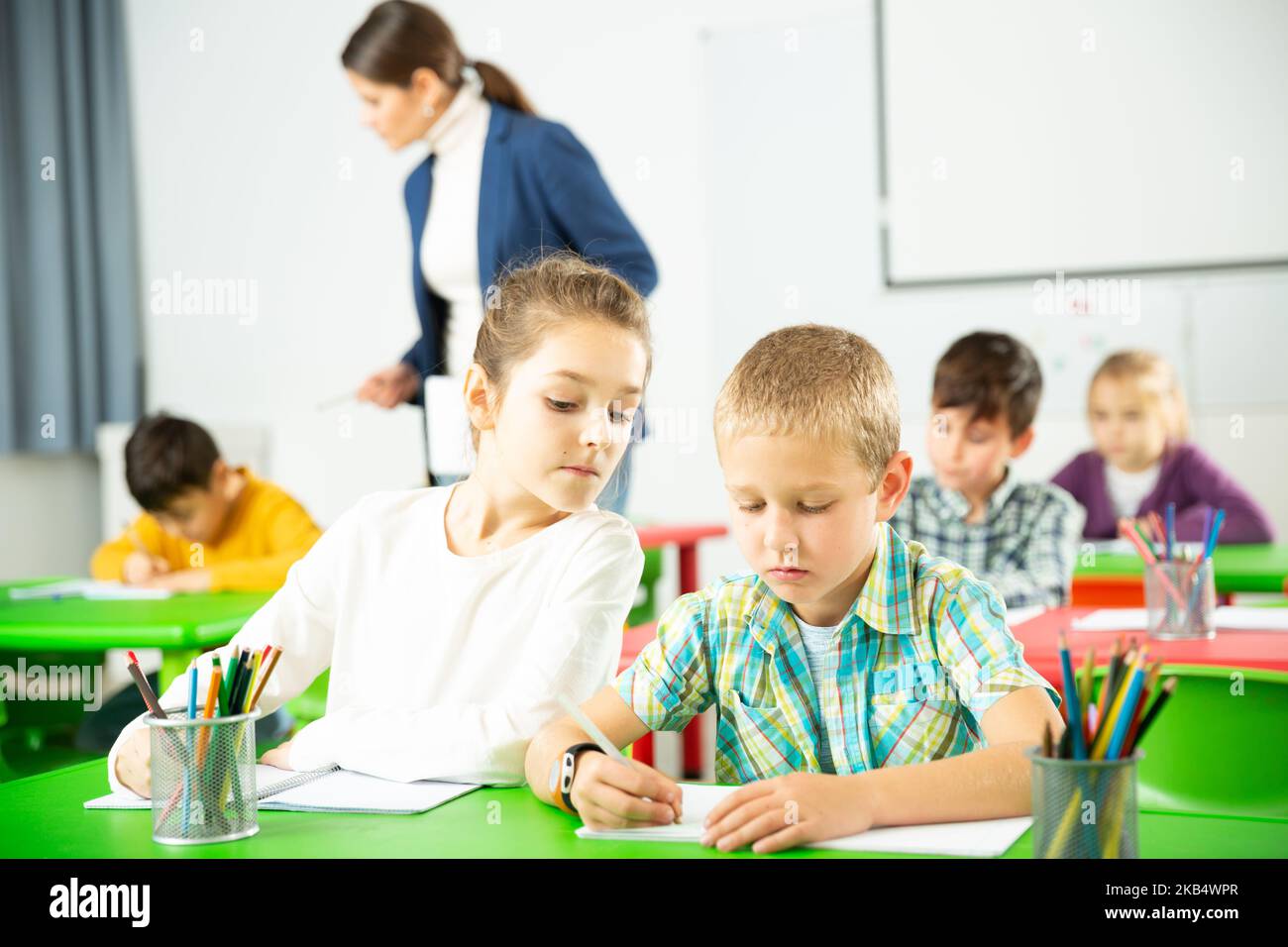 Les élèves heureux assis bavardant à leçon à l'école élémentaire Banque D'Images