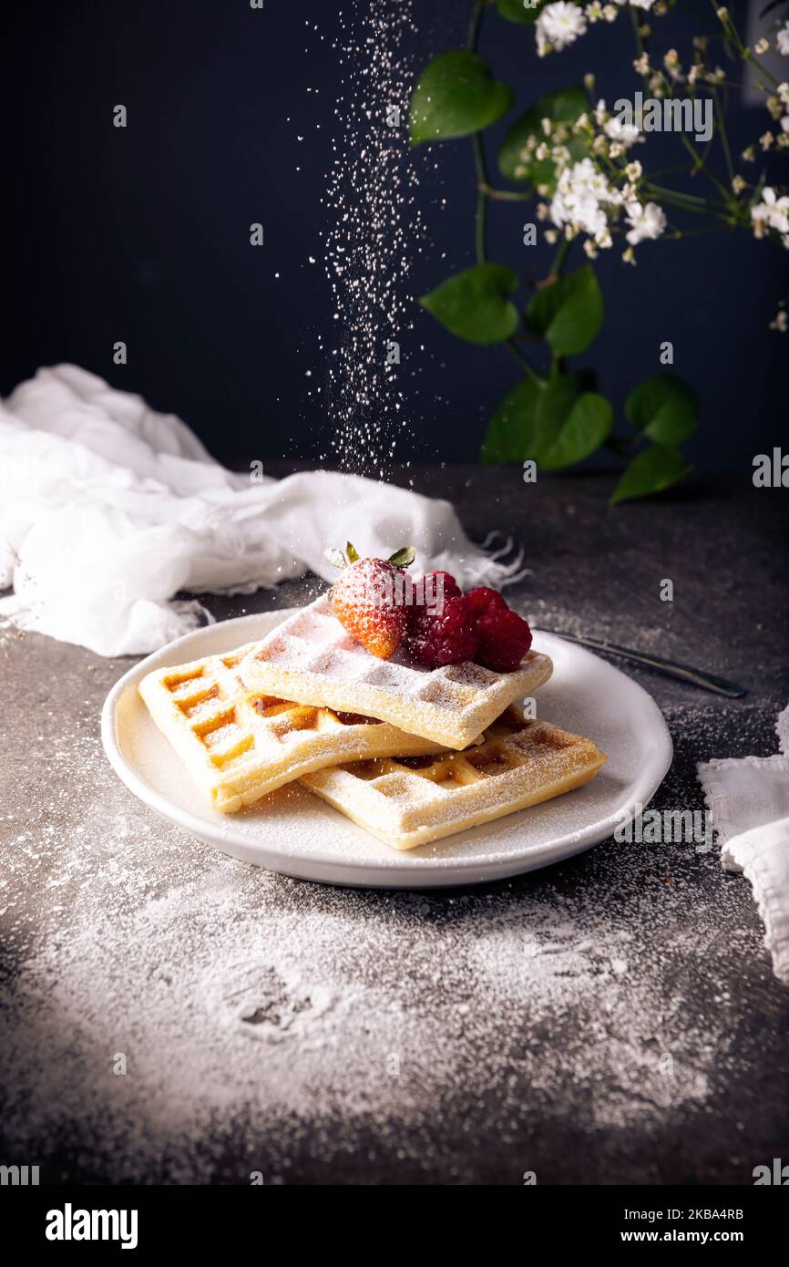 Gaufres maison sucrées avec fraises, framboises et sucre en poudre sur un plat blanc. Banque D'Images