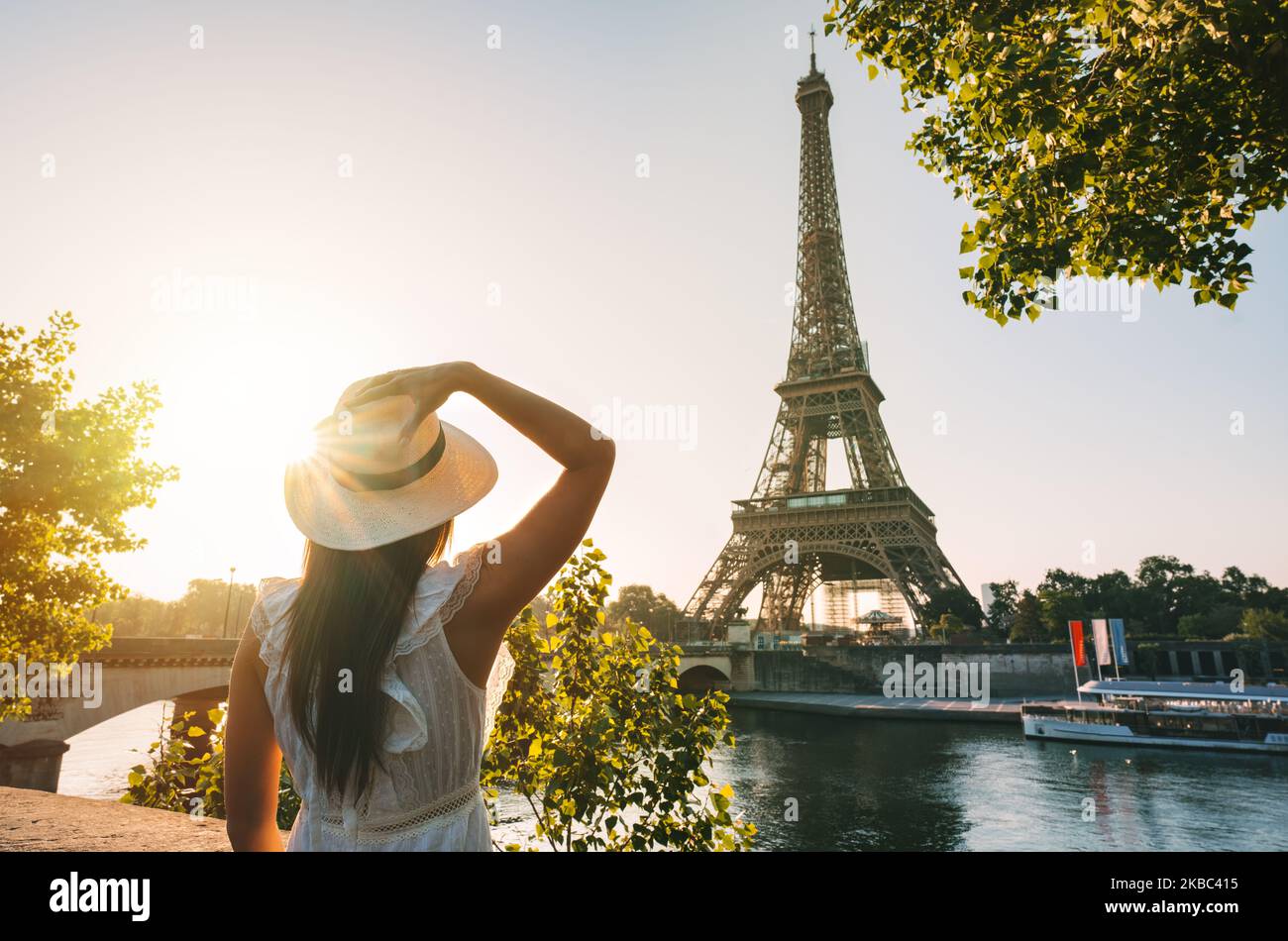 Jeune femme touriste en chapeau de soleil et robe blanche debout devant la Tour Eiffel à Paris au coucher du soleil. Voyage en France, concept de tourisme Banque D'Images