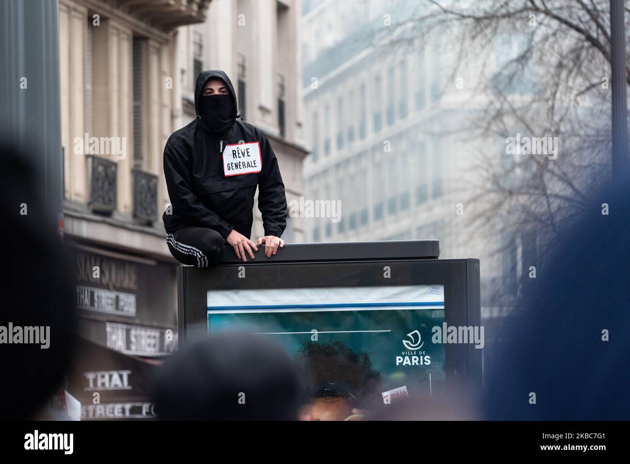 Un démonstrateur à bloc noir avec un autocollant « rêve général » collé sur  lui observe les affrontements qui se sont déroulés au-dessus d'un panneau  d'affichage jeudi, 5 décembre 2019, le premier