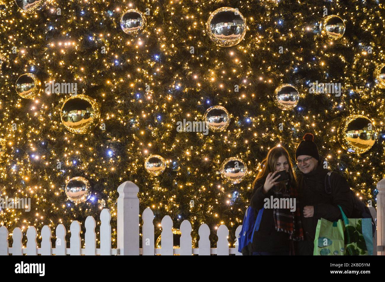 Les gens prennent des selfies devant un arbre de Noël devant la gare principale de Cracovie et le centre commercial Galeria Krakowska Shoping. Lundi, 16 décembre 2019, à Cracovie, petite Pologne Voivodeship, Pologne. (Photo par Artur Widak/NurPhoto) Banque D'Images
