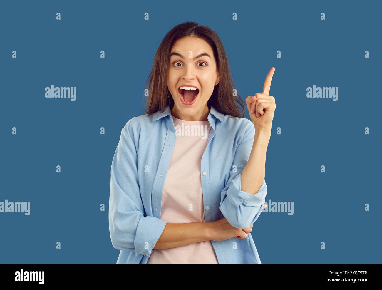 La femme a une bonne idée, pointe vers le haut et regarde la caméra avec l'expression de visage heureux excité Banque D'Images