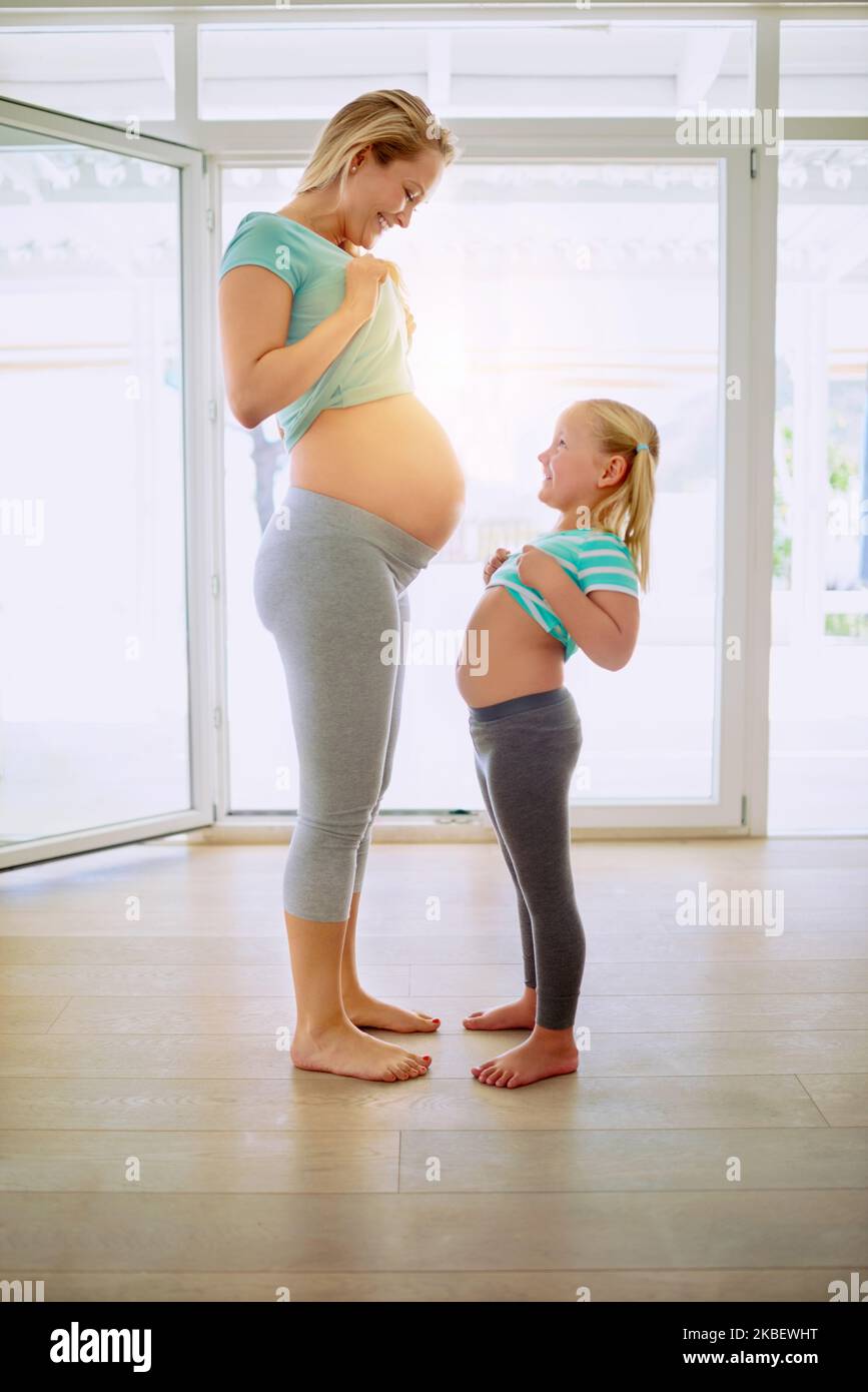 Voulez-vous voir mon ventre aussi. Une femme enceinte et sa petite fille se montrant leurs estomacs à la maison. Banque D'Images