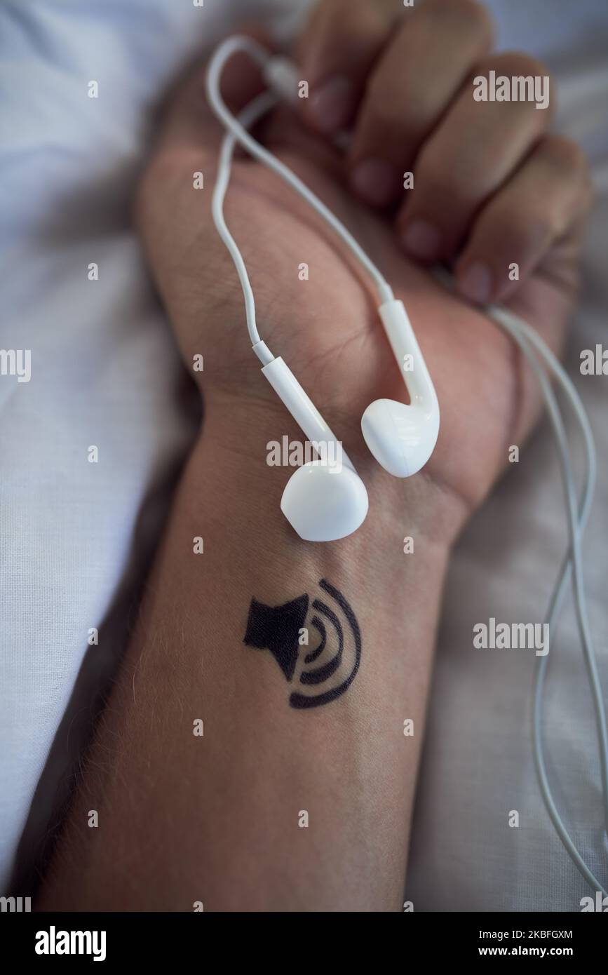 La musique me fait échapper. Des écouteurs dans une personne méconnaissable se ferment les mains et un tatouage d'un haut-parleur sur son poignet. Banque D'Images