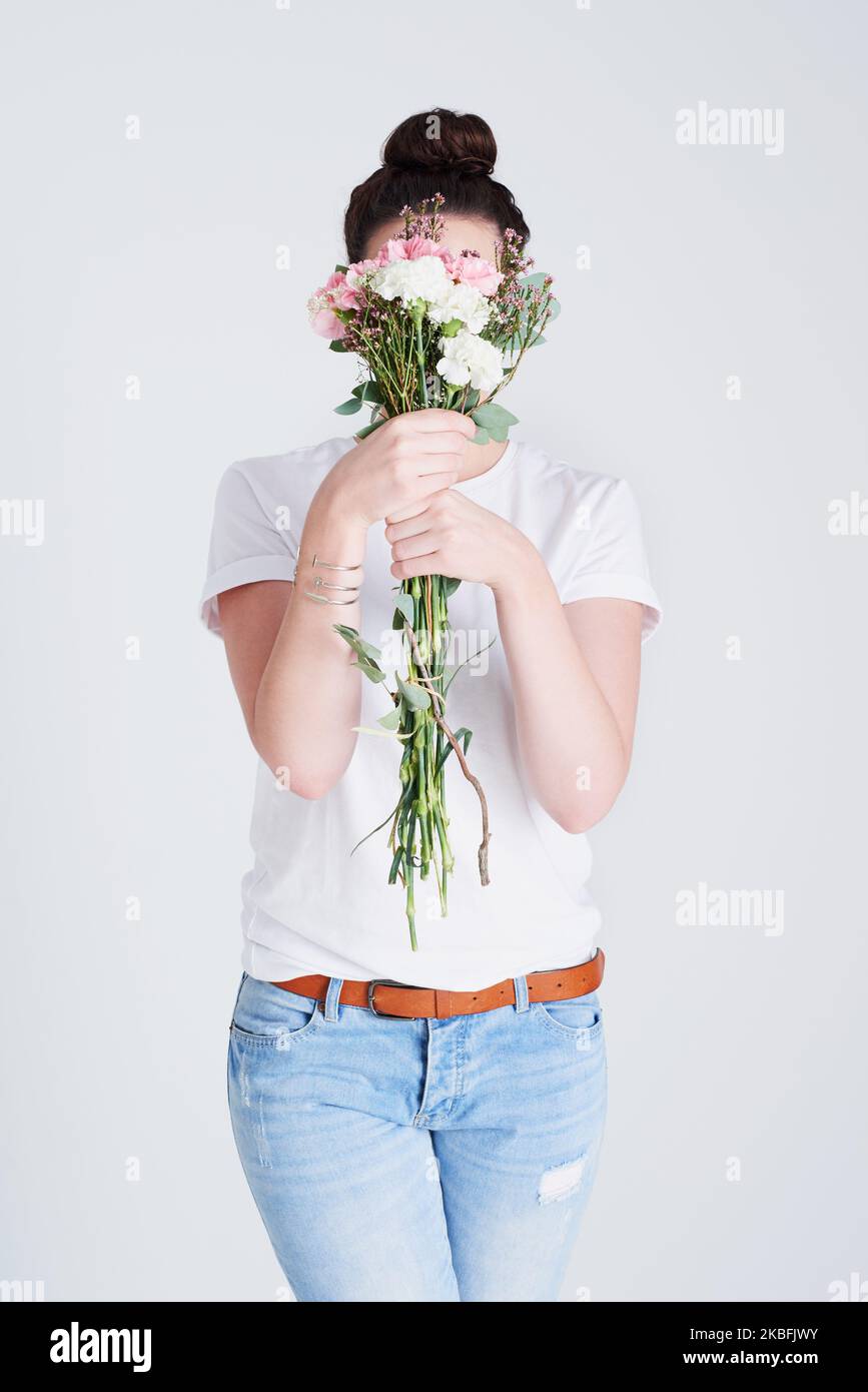 Il est facile de se cacher derrière de belles fleurs. Photo studio d'une femme méconnue couvrant son visage de fleurs sur fond gris. Banque D'Images