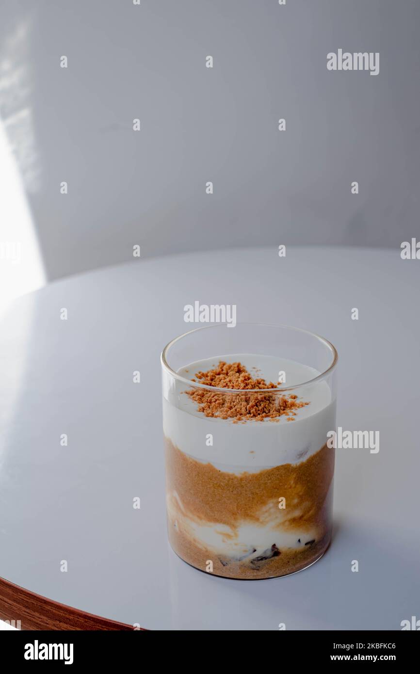 Un verre de café au lait crème fouetté et à la garniture de cachets broyés qui se répandit sur la surface dans une table blanche près de la fenêtre Banque D'Images