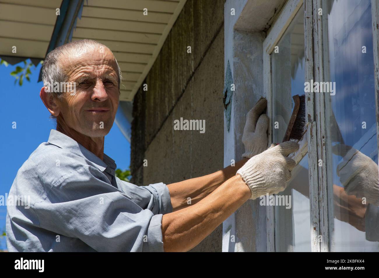 Un portrait d'un retraité brosse la fenêtre de l'ancienne peinture blanche Banque D'Images