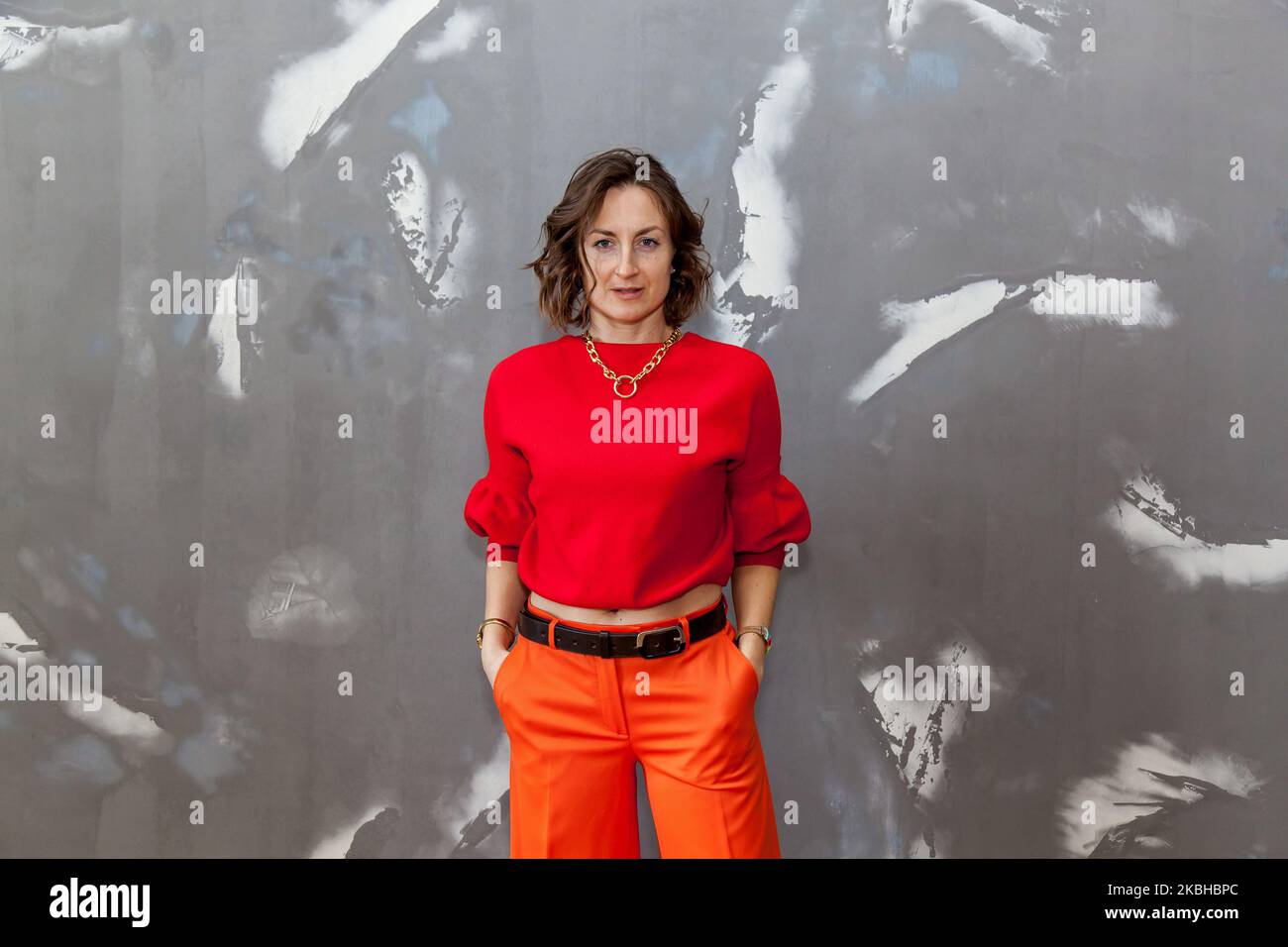 Fille tendance et élégante posant dans un pantalon orange, un chandail rouge contre un mur gris Banque D'Images