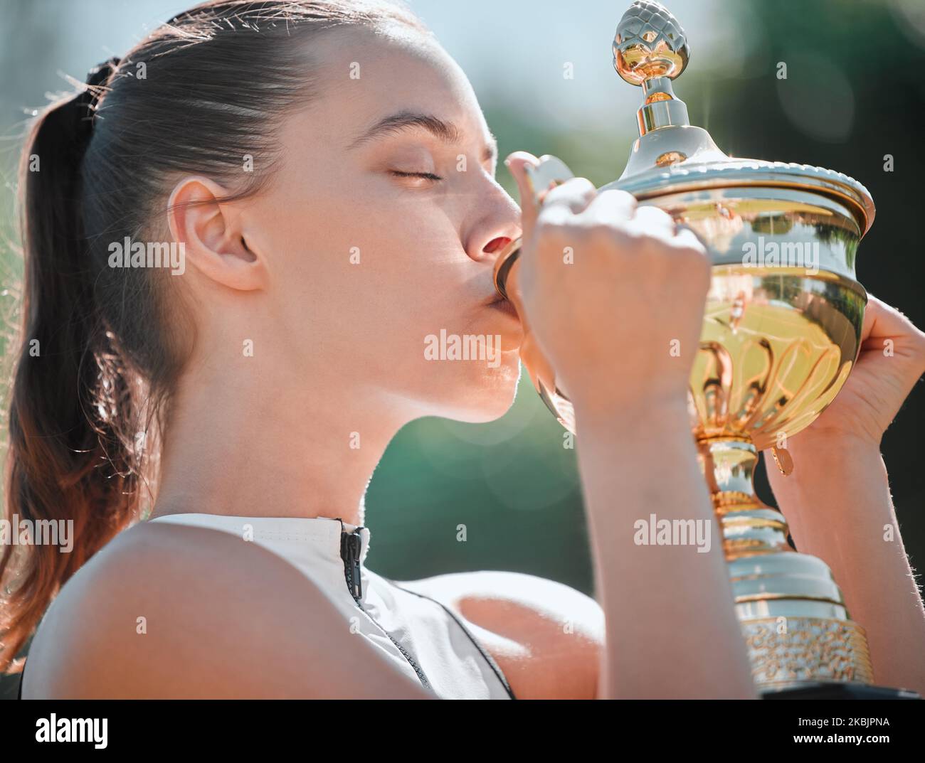 Sport, gagnant et femme baiser trophée après le succès du jeu de tennis avec la réalisation de sports et de remise en forme en plein air. Faites de l'exercice, gagnez et fêtez les jeunes athlètes Banque D'Images