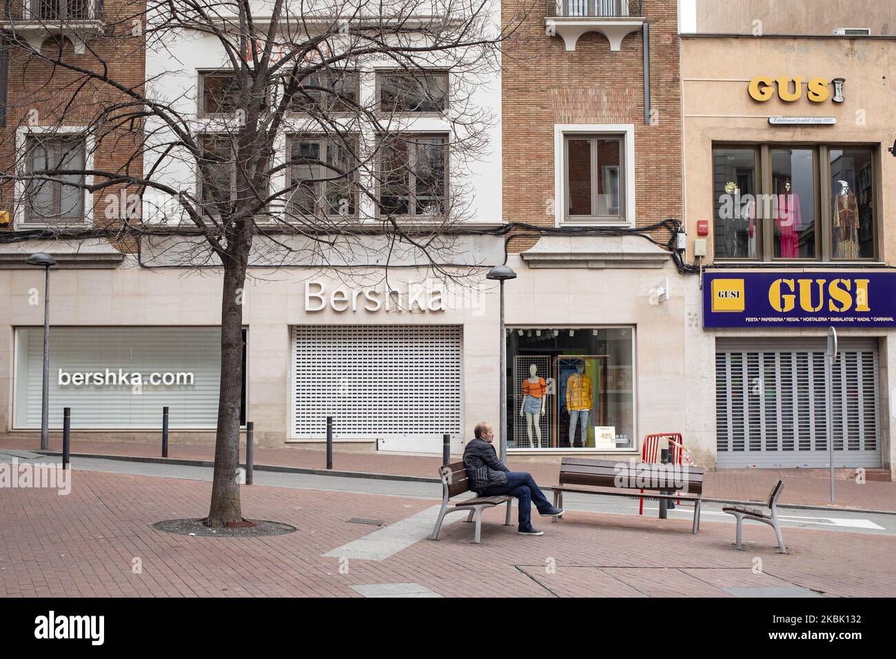Un homme reposant sur un banc avec Bershka et Gusi magasins fermés après  l'état d'alarme imposé par le gouvernement espagnol et mesure de  verrouillage de la population de Catalogne par le gouvernement
