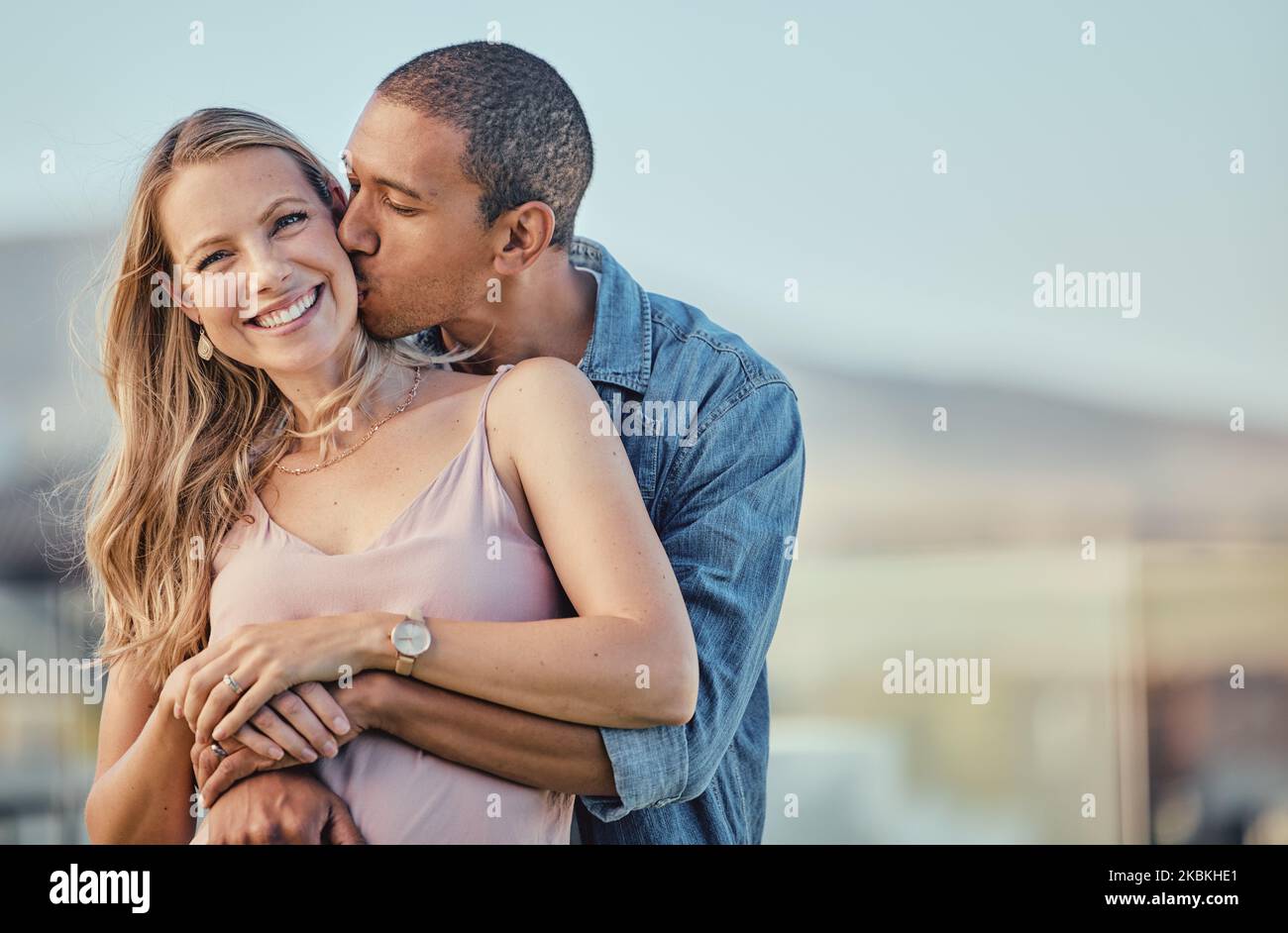Couple, baiser et sourire de personnes avec un câlin ensemble extérieur sentiment amour, soin et bonheur. Portrait du mariage, engagement et heureux interracial Banque D'Images