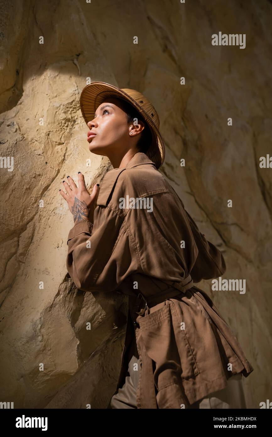 archéologue en blouson beige et chapeau de safari en regardant loin près de la roche dans la grotte, image de stock Banque D'Images