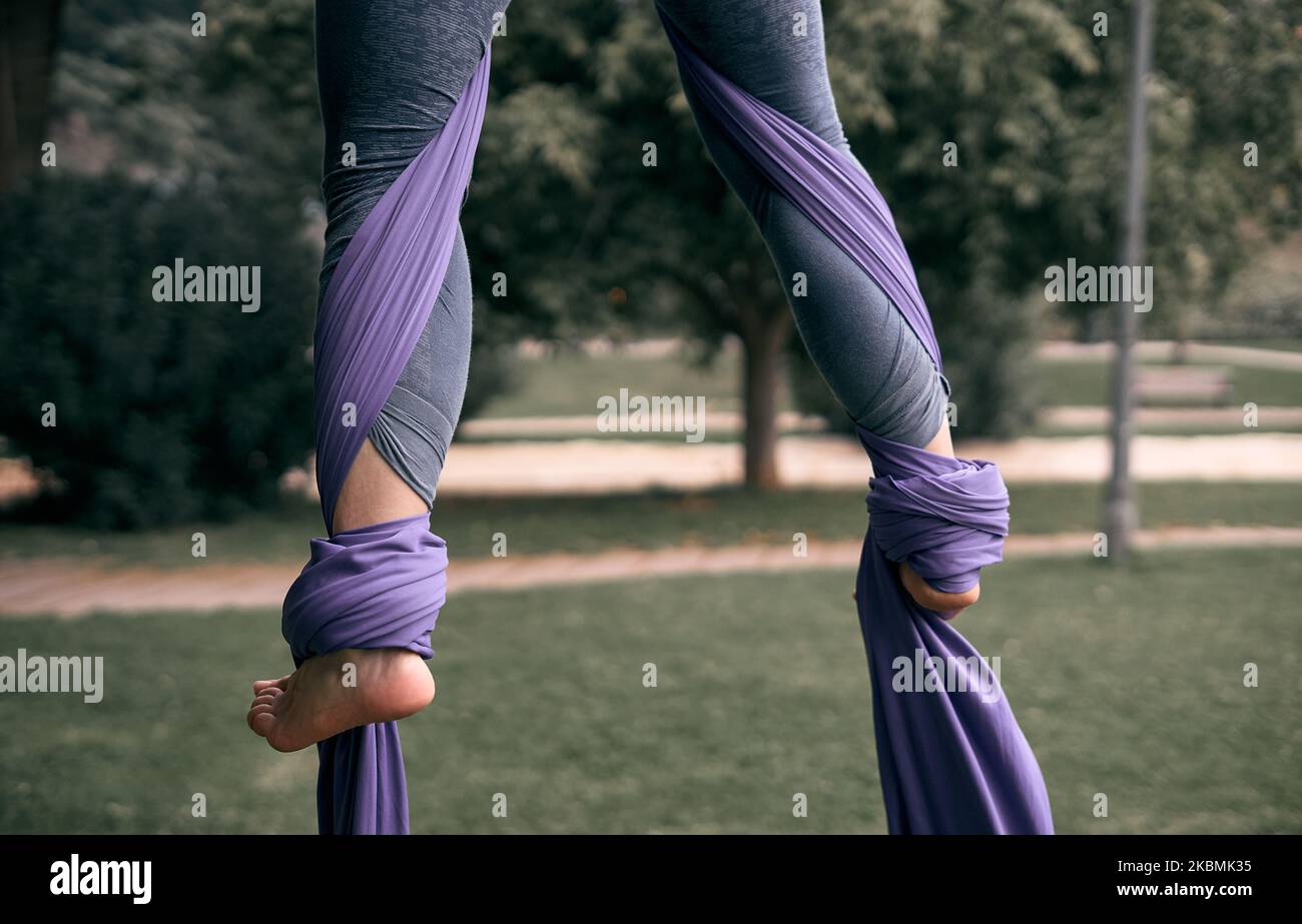 Jeune femme caucasienne pratiquant des silks aériens sur un pont dans une ville de parc, entourée par la nature. Banque D'Images