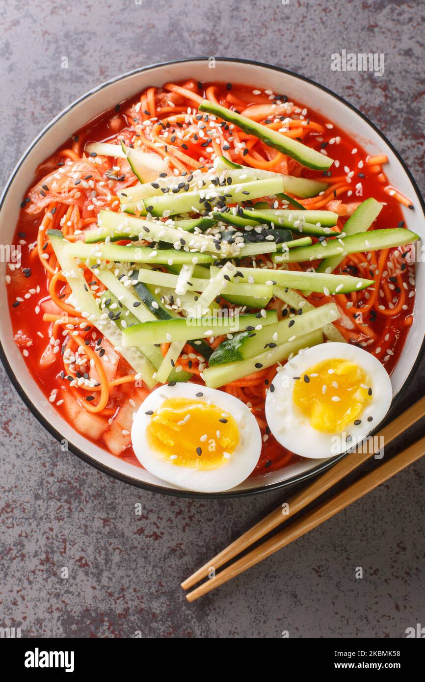 Salade coréenne de nouilles froides ou bibium guksu, garnie d'œufs durs, de sésame et de concombre dans le bol de la table. Vue verticale du dessus Banque D'Images