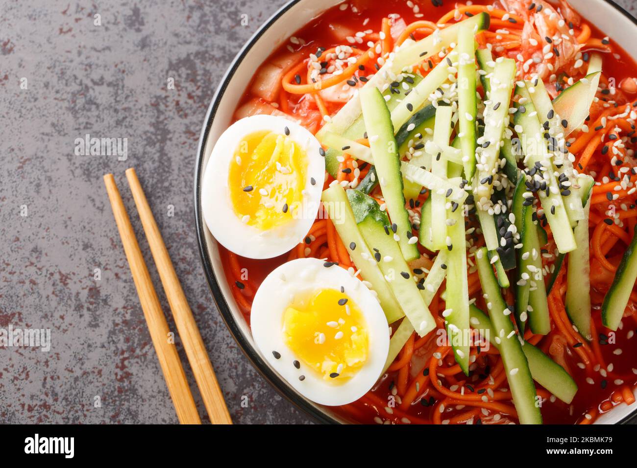 Salade de nouilles épicées coréennes Bibim-guksu avec kimchi, concombre et oeufs dans le bol de la table. Vue horizontale du dessus Banque D'Images
