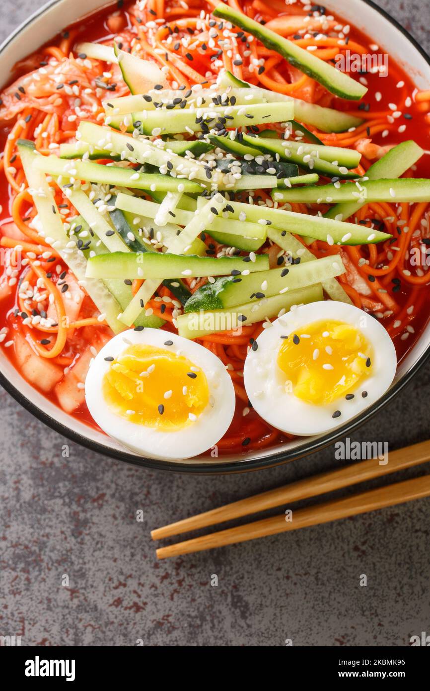 Nouilles Spicy coréennes Bibim Guksu ontop oeuf cuit traditionnel nourriture populaire plat fermé dans le bol sur la table. Vue verticale du dessus Banque D'Images