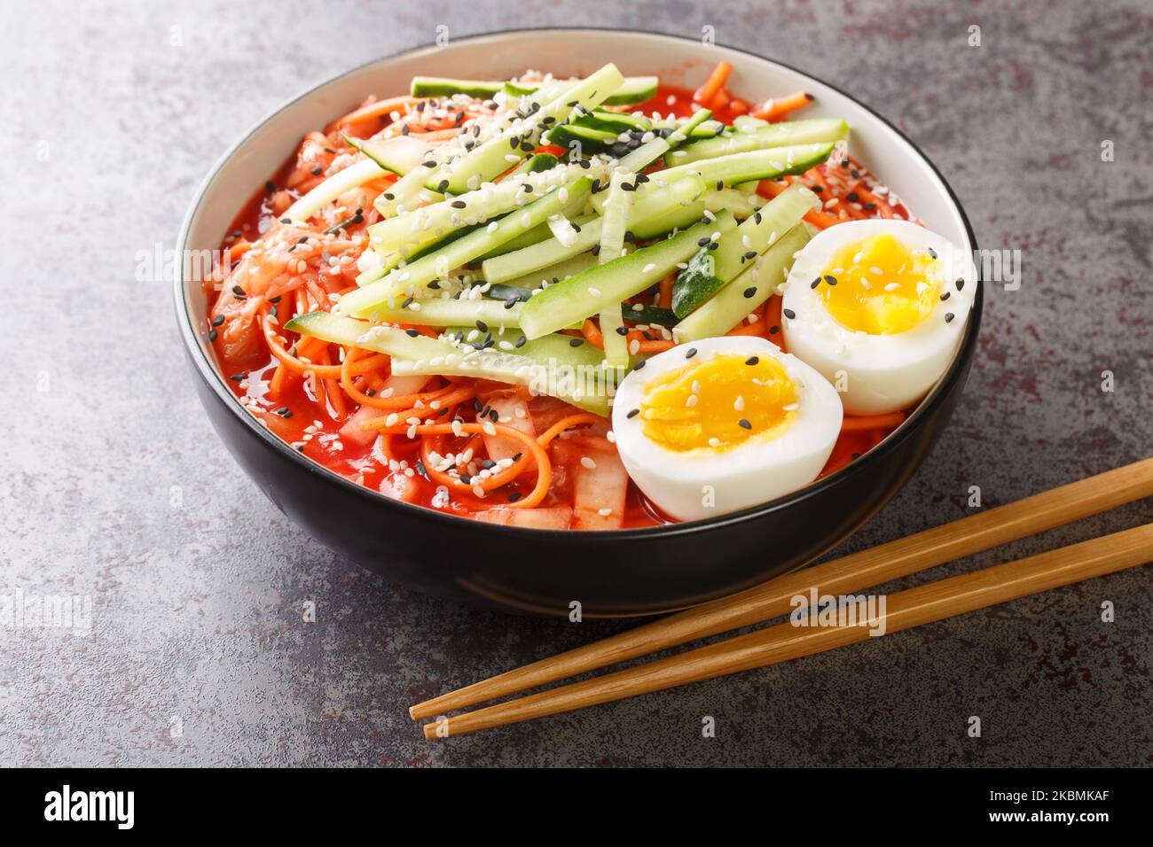 Salade de nouilles épicées coréennes Bibim-guksu avec kimchi, concombre et oeufs dans le bol de la table. Horizontale Banque D'Images