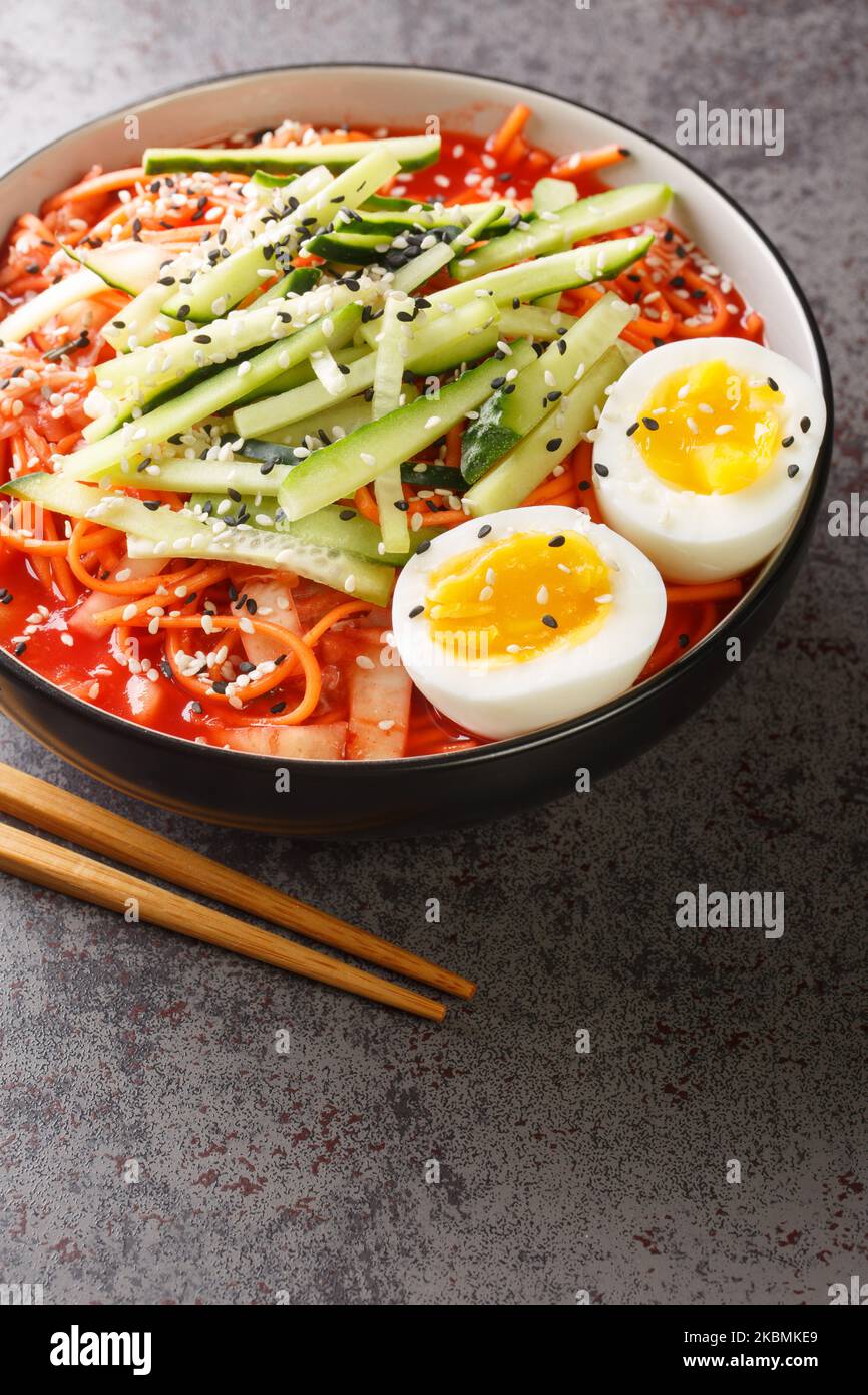 Nouilles Spicy coréennes Bibim Guksu ontop oeuf cuit traditionnel nourriture populaire plat fermé dans le bol sur la table. Verticale Banque D'Images