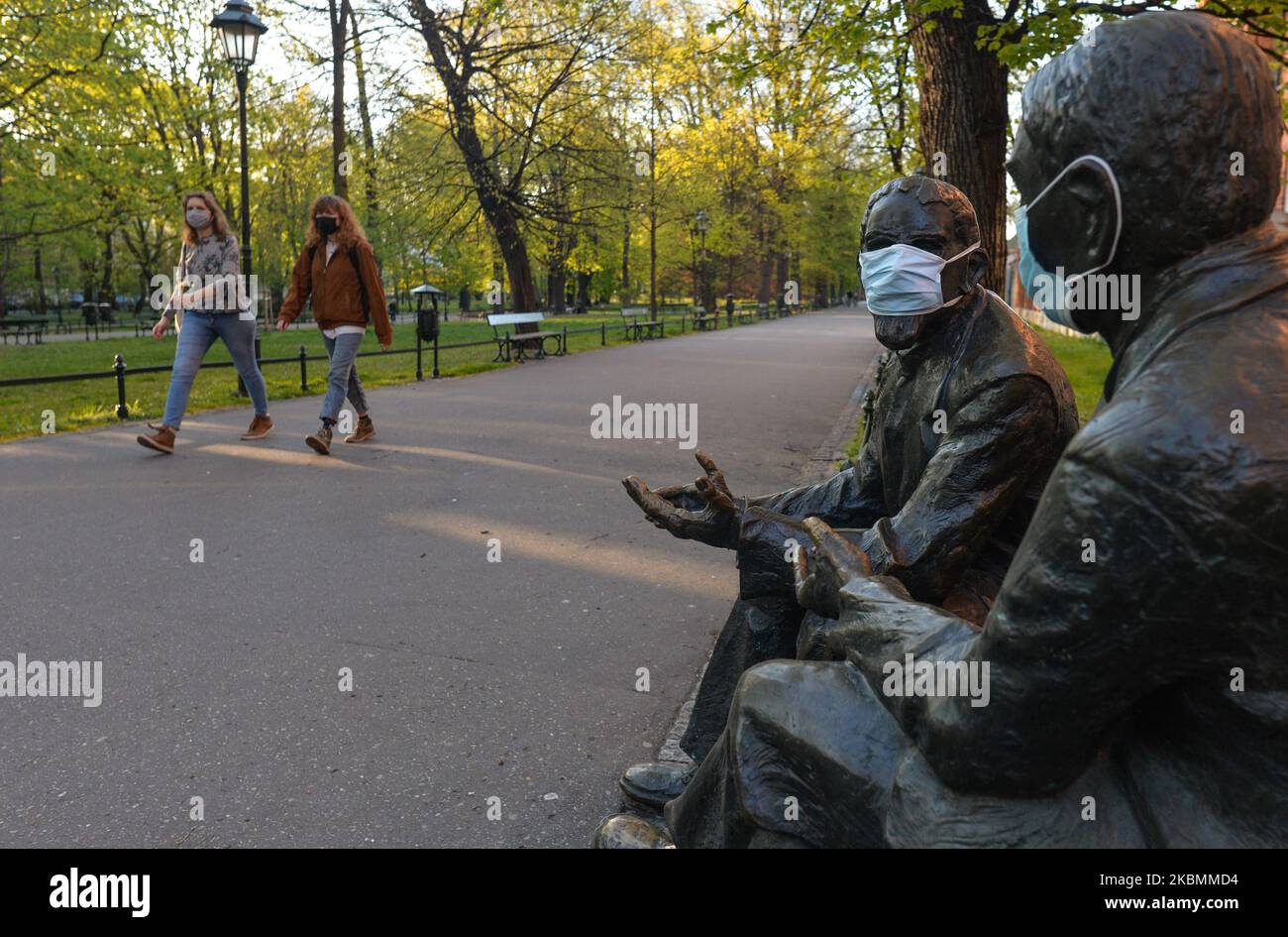 Deux jeunes femmes marchent à côté d'une statue de Stefan Banach et d'Otton Nikodym avec des masques médicaux vus dans le parc Planty de Cracovie, car les Polonais peuvent à nouveau profiter de l'espace vert. A partir d'aujourd'hui (20 avril), l'interdiction de se déplacer, de voyager et de séjourner dans les lieux publics a été levée. Les parcs publics, les forêts et les plages ont été rouverts, à l'exception des terrains de jeux et des installations sportives. Les enfants de plus de 13 ans peuvent se déplacer sans parents. La couverture de la bouche et du nez en public reste obligatoire. Les terrains de jeux et les installations sportives restent fermés. Lundi, 20 avril 2020, à Cracovie, en Pologne. (Photo par Artur Widak/NURP Banque D'Images