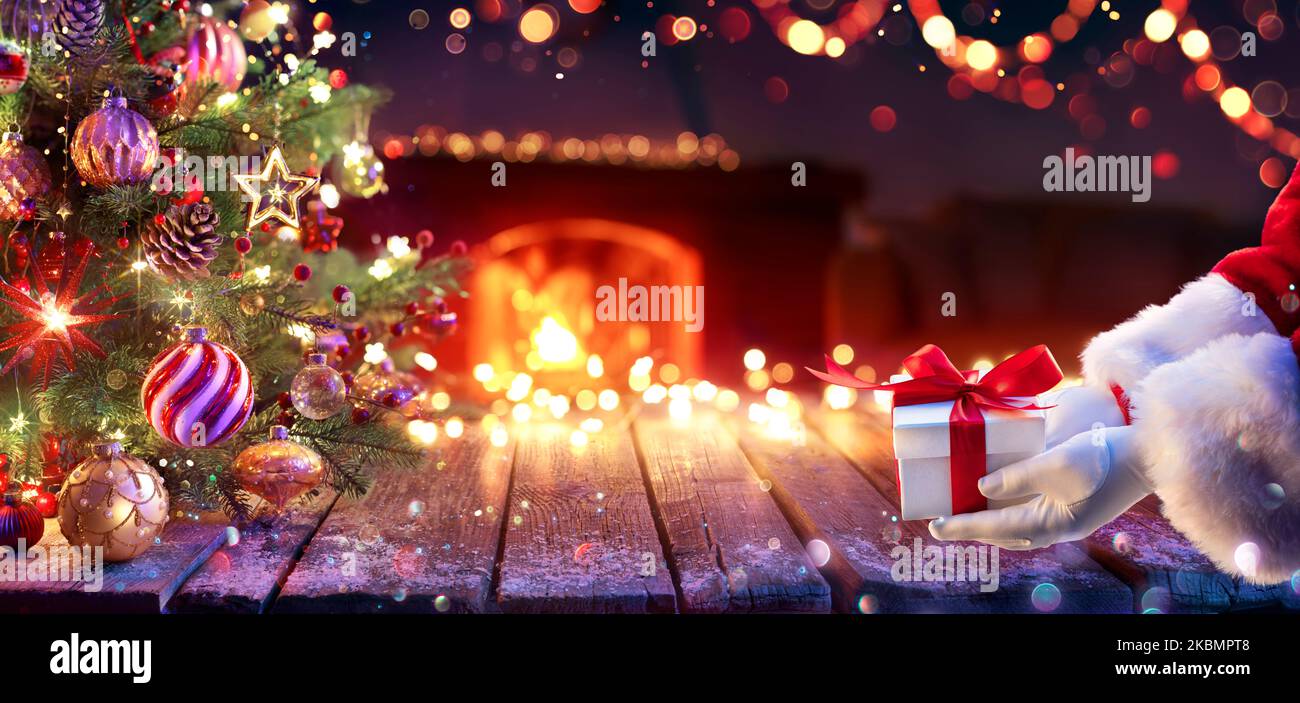 Le Père Noël donne le cadeau sous le sapin de Noël - boîte cadeau et décoration dans la maison intérieure avec des lumières diffus abstraites la nuit Banque D'Images