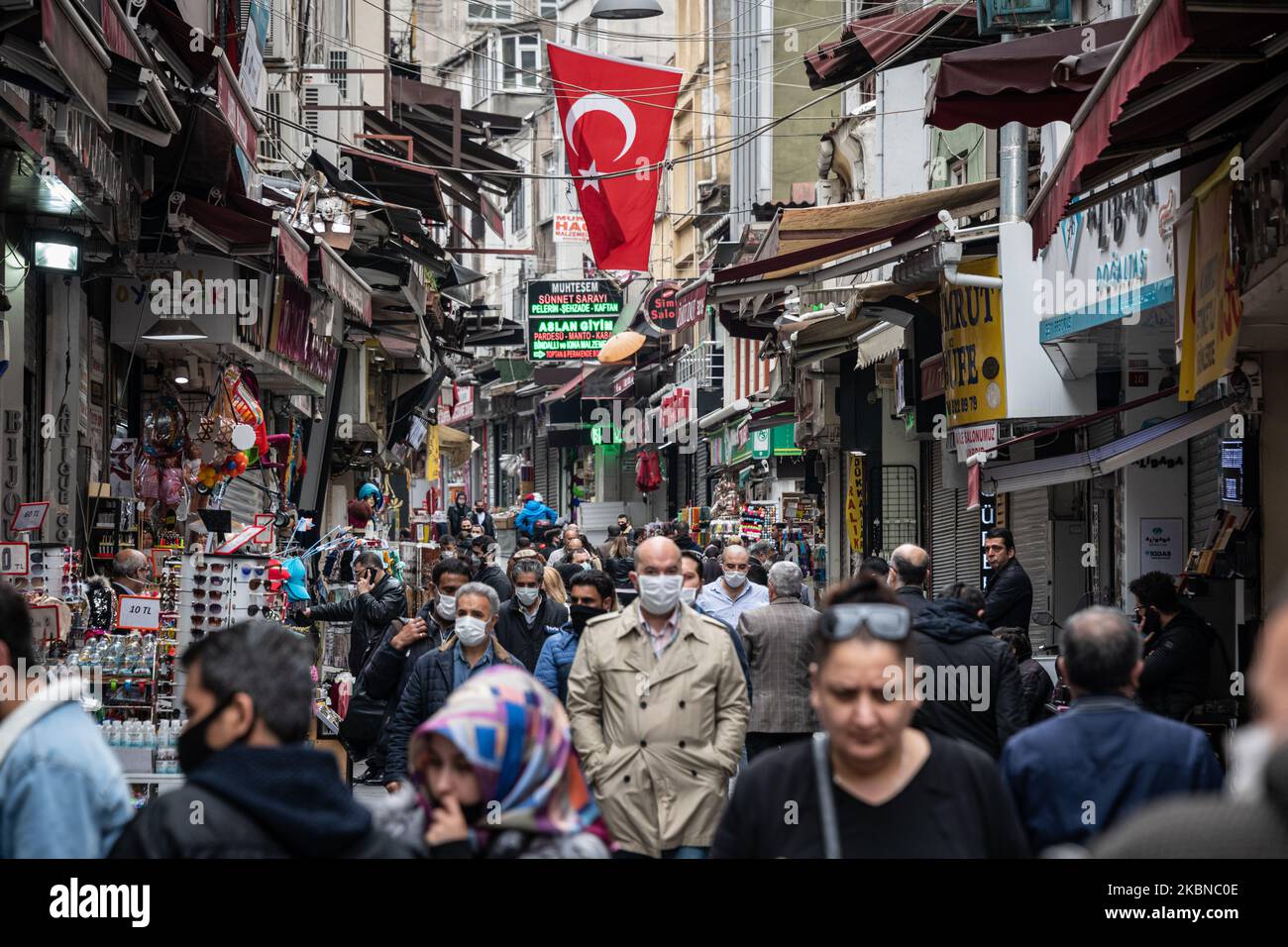 Le 5 mai 2020, les résidents d'Istanbul, le centre de la pandémie de Covid-19 en Turquie, portaient des masques lorsqu'ils magasinaient dans le quartier historique d'Eminonu, où de nombreux magasins restent fermés en raison des restrictions imposées pour enrayer la propagation du coronavirus. De telles précautions pèsent lourdement sur l'économie turque et sur la lire turque, qui est tombée à sa plus faible valeur depuis la crise financière de cette semaine. Ci-dessus, les acheteurs turcs portant des masques marchent sous un drapeau turc dans une zone de marché bondée dans le quartier Eminonu de Fatih, Istanbul. (Photo de Diego Cupolo/NurPhoto) Banque D'Images