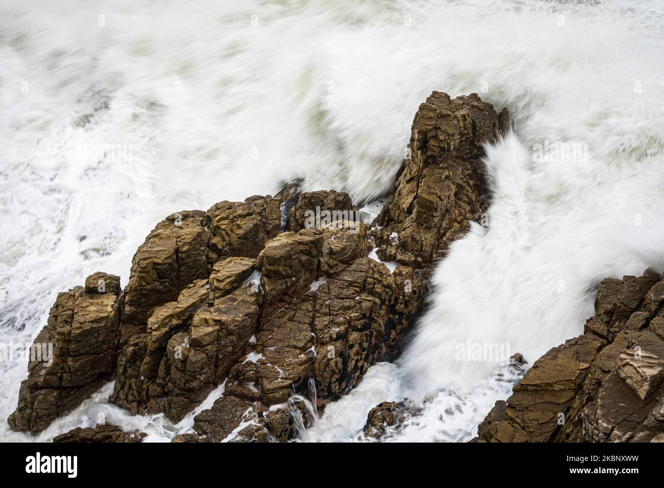 Une vague de l'océan s'écrasant sur des rochers le long de la côte d'Hermanus, le mouvement a erré en raison de la vitesse d'obturation lente. Whale Coast, Overberg, Western Banque D'Images