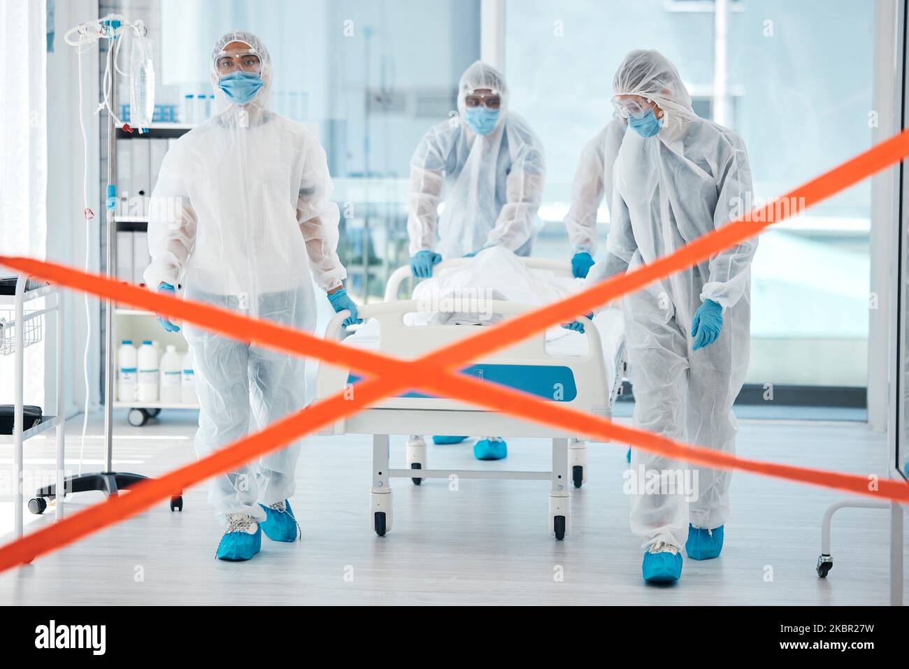 Quarantaine Covid, équipe médicale et patient au lit, se déplaçant vers une zone d'isolement ou de test avec ruban d'avertissement à l'hôpital. EPI, sécurité et soins de santé Banque D'Images