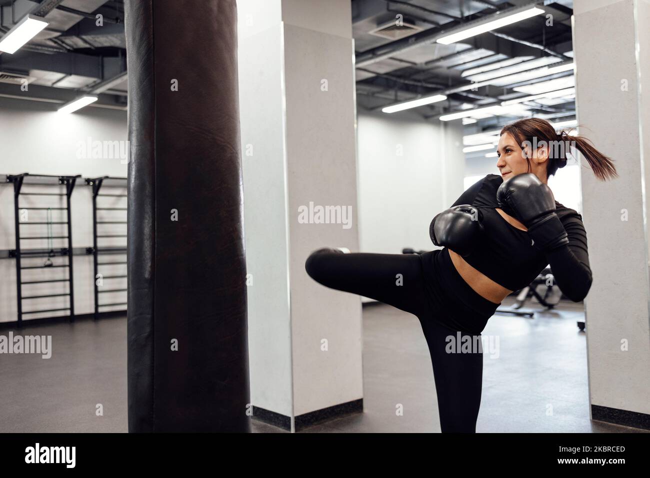 Une femme de boxe latine forte saute de coup de pied à un énorme sac de poinçonnage à la salle de fitness. Entraînement de fille athlétique Muay Thai boxe pour le culturisme et la vie saine Banque D'Images