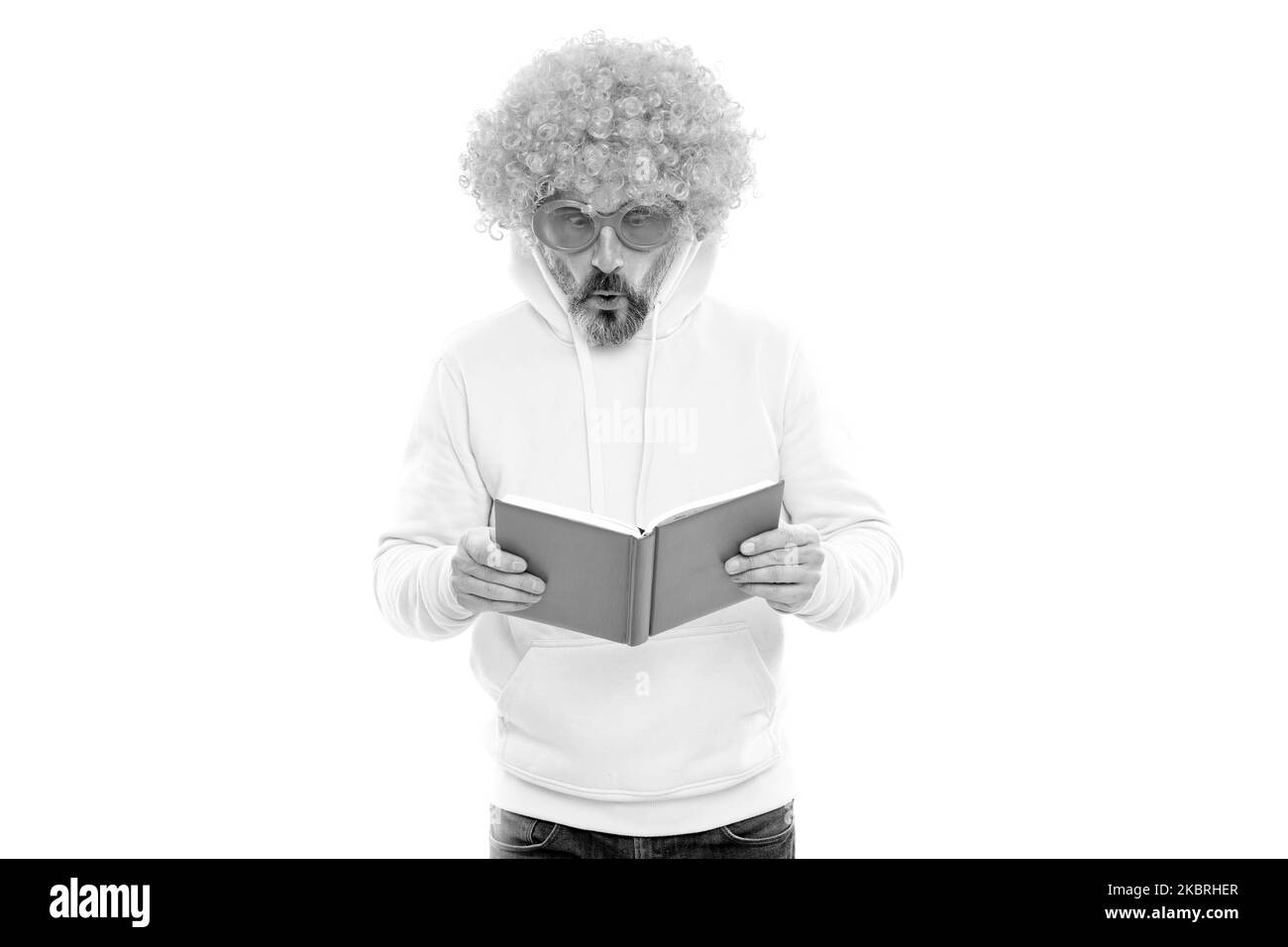 Étudiant senior dans la perruque funky lire le livre d'école dans des lunettes de soleil avec le regard surpris, la connaissance Banque D'Images