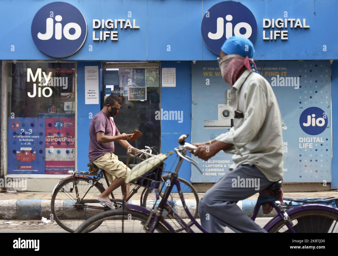 Personnes sur des passes à vélo par un magasin de Jio à Kolkata, Inde, 13 juillet, 2020. Dimanche, selon un rapport des médias indiens, Reliance Industries a déclaré que Qualcomm Inc achètera 0,15 % de ses plates-formes numériques Jio pour 7,3 milliards de roupies (97,1 millions de dollars). (Photo par Indranil Aditya/NurPhoto) Banque D'Images