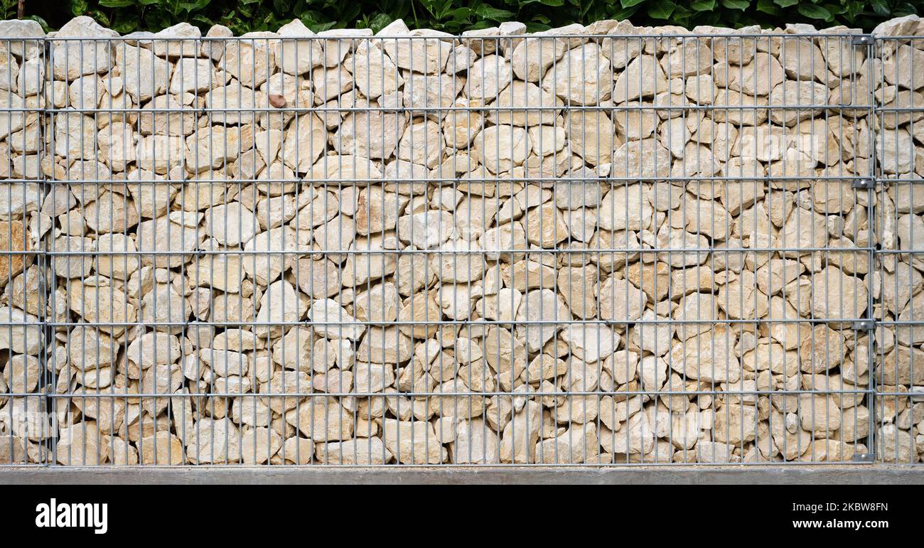 Les pierres naturelles beige clair sont soigneusement superposées dans un mur de gabion galvanisé. Banque D'Images