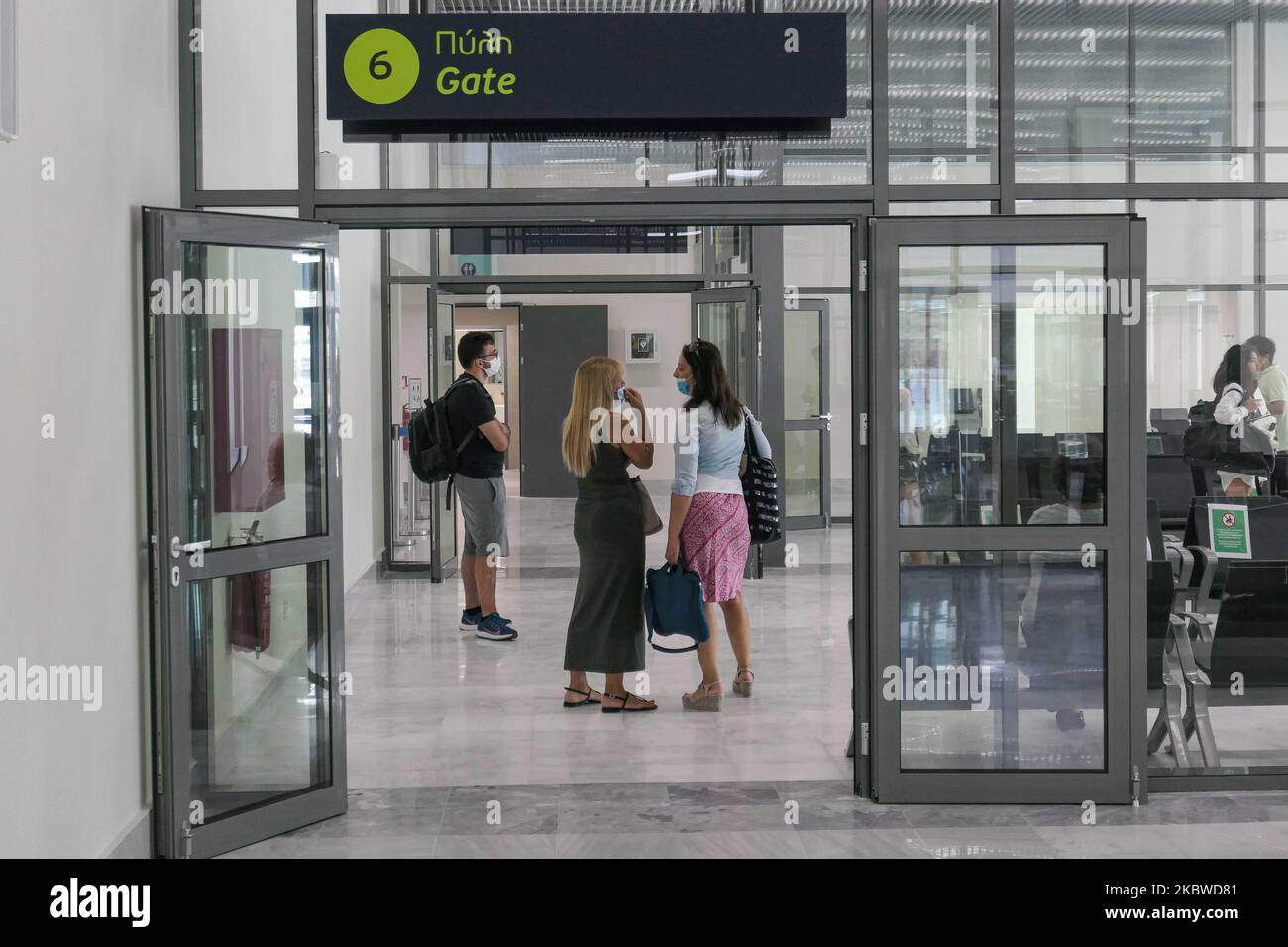 Les passagers féminins qui parlent en portant un masque facial sous les panneaux Gate 6 avant d'embarquer. Vol au départ de l'aéroport international de Mykonos JMK LGMK en Grèce. Les passagers munis de masques faciaux et de mesures de protection comme gants, désinfectant pour les mains, sièges bloqués, signes sociaux de distanciation, etc. En raison des mesures de sécurité contre la pandémie du coronavirus Covid-19, telles qu'elles sont observées aux comptoirs d'enregistrement, au terminal principal de départ, aux portes et en se rapprochant de l'avion, Un avion turbopropulseur Olympic Air Bombardier DHC-8-400 avec enregistrement SX-OBA. L'aéroport appartient au gouvernement grec mais est exploité par Fraport Grèce Banque D'Images