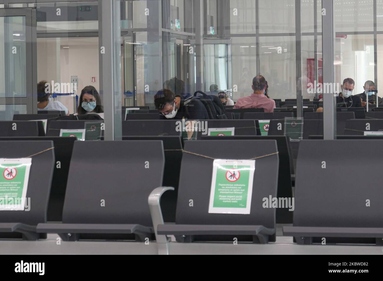 Passagers et sièges vides avec des panneaux les bloquant à l'intérieur de la zone des portes avant l'embarquement. Vol au départ de l'aéroport international de Mykonos JMK LGMK en Grèce. Les passagers munis de masques faciaux et de mesures de protection comme gants, désinfectant pour les mains, sièges bloqués, signes sociaux de distanciation, etc. En raison des mesures de sécurité contre la pandémie du coronavirus Covid-19, telles qu'elles sont observées aux comptoirs d'enregistrement, au terminal principal de départ, aux portes et en se rapprochant de l'avion, Un avion turbopropulseur Olympic Air Bombardier DHC-8-400 avec enregistrement SX-OBA. L'aéroport appartient au gouvernement grec mais est exploité par Fraport Greec Banque D'Images