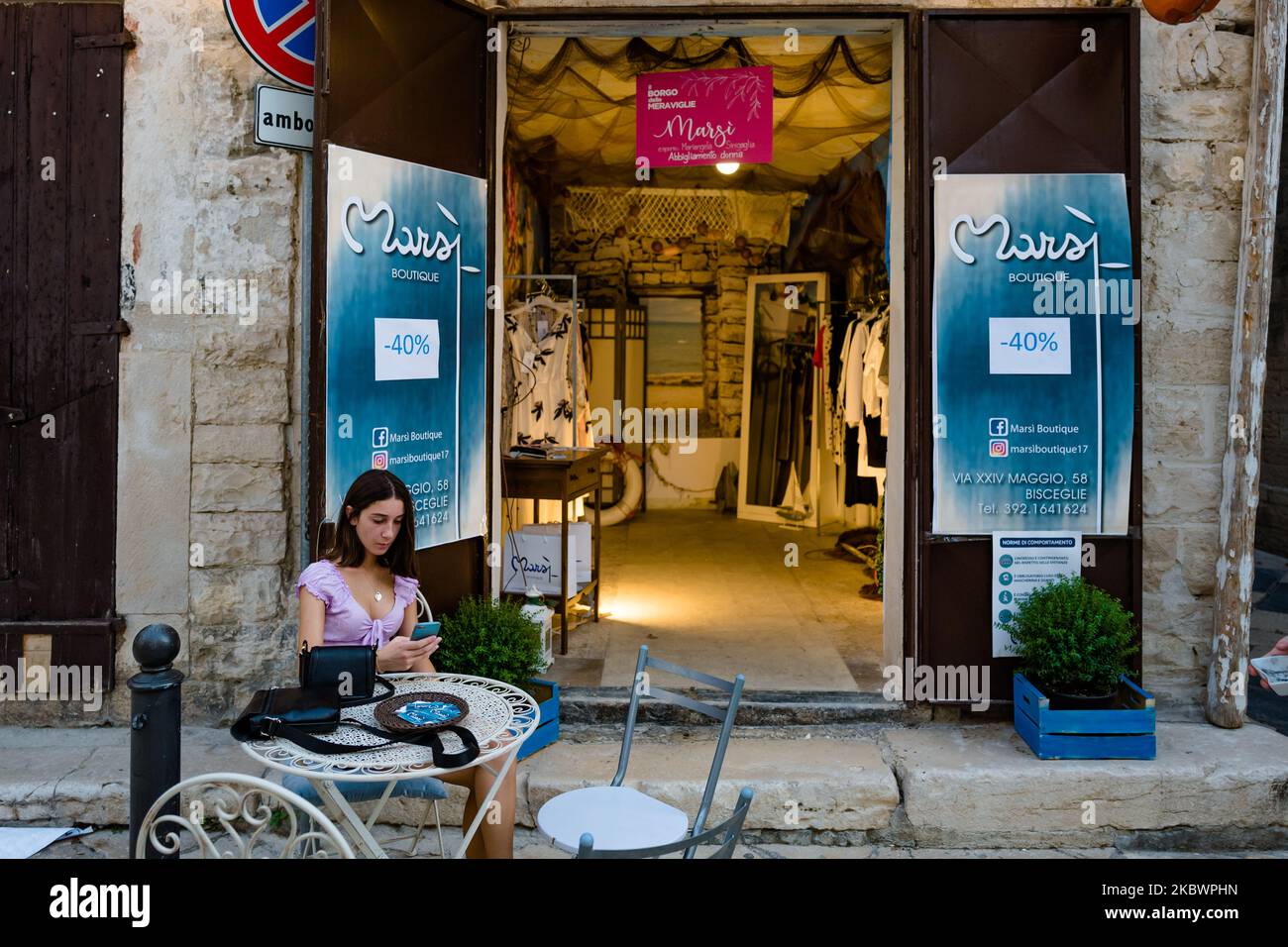 Une fille assise devant son magasin de vêtements dans le centre historique de Bisceglie sur 4 août 2020. A l'occasion de l'été, dans la ville de Bisceglie, ils ont organisé 'Borgo delle Meraviglie', un événement pour redécouvrir et raviver le centre historique et les locaux du Borgo Antico, trop longtemps abandonné qui a accueilli la présence de marchands, d'artistes et d'artisans. (Photo par Davide Pischettola/NurPhoto) Banque D'Images