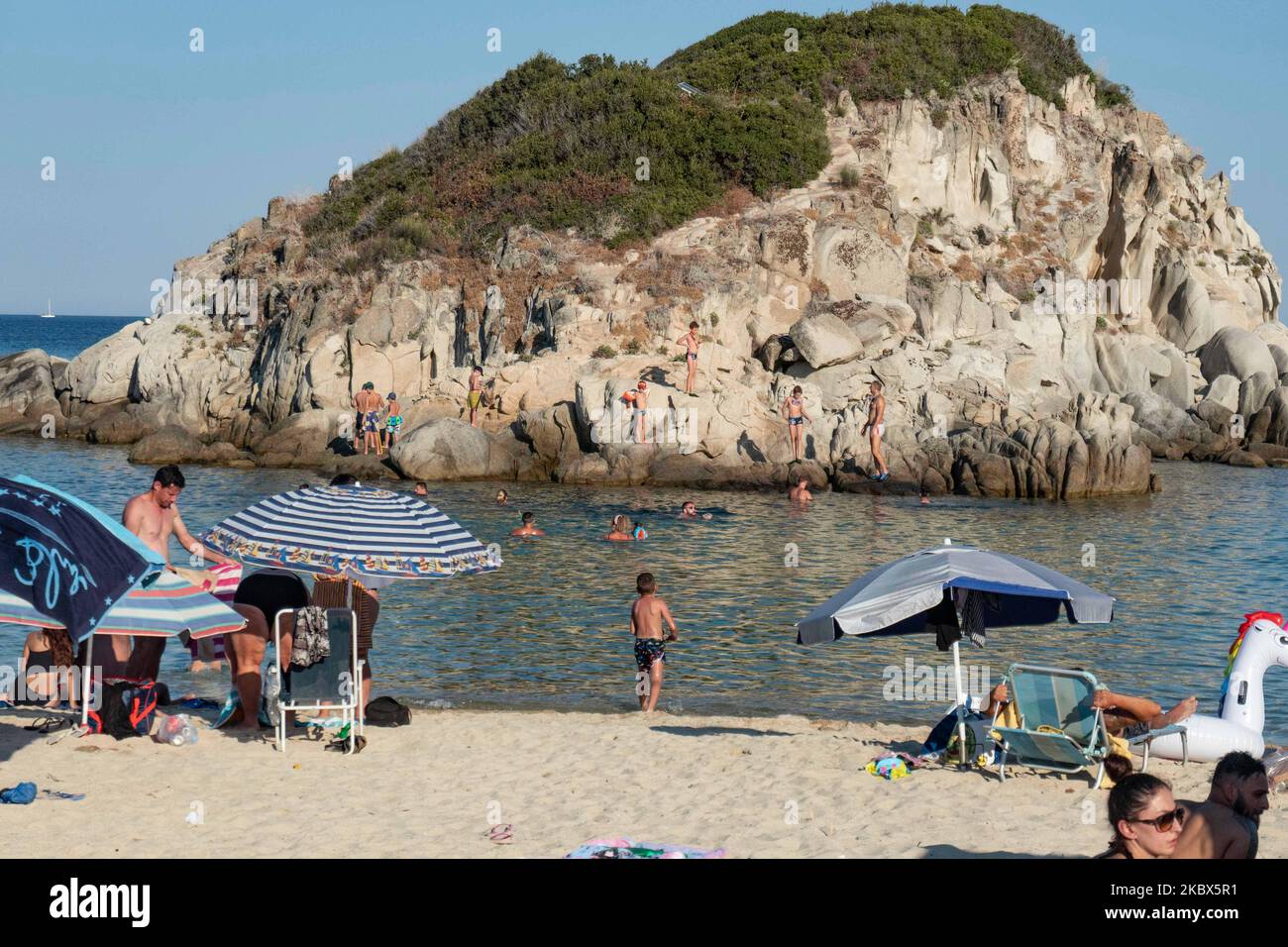 La petite île près de la rive de Kalamitsi. Foule de touristes à la célèbre et populaire plage de Kalamitsi située à la pointe sud de la péninsule de Sithonia à Chalkidiki dans le nord de la Grèce. Les gens s'amusent à la plage en Grèce car ils se détendent à l'ombre des parasols, plongée en apnée, plongée sous-marine, natation dans les eaux cristallines tropicales exotiques, sports nautiques, location de bateaux, prendre un verre dans les bars de la plage ou prendre un bain de soleil sur le sable doré et profiter de la vie sur la plage sous le ciel bleu ensoleillé. Il y a une petite île également située près de la rive. Le gouvernement local Banque D'Images