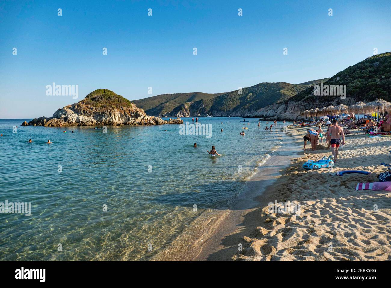 La petite île près de la rive de Kalamitsi. Foule de touristes à la célèbre et populaire plage de Kalamitsi située à la pointe sud de la péninsule de Sithonia à Chalkidiki dans le nord de la Grèce. Les gens s'amusent à la plage en Grèce car ils se détendent à l'ombre des parasols, plongée en apnée, plongée sous-marine, natation dans les eaux cristallines tropicales exotiques, sports nautiques, location de bateaux, prendre un verre dans les bars de la plage ou prendre un bain de soleil sur le sable doré et profiter de la vie sur la plage sous le ciel bleu ensoleillé. Il y a une petite île également située près de la rive. Le gouvernement local Banque D'Images