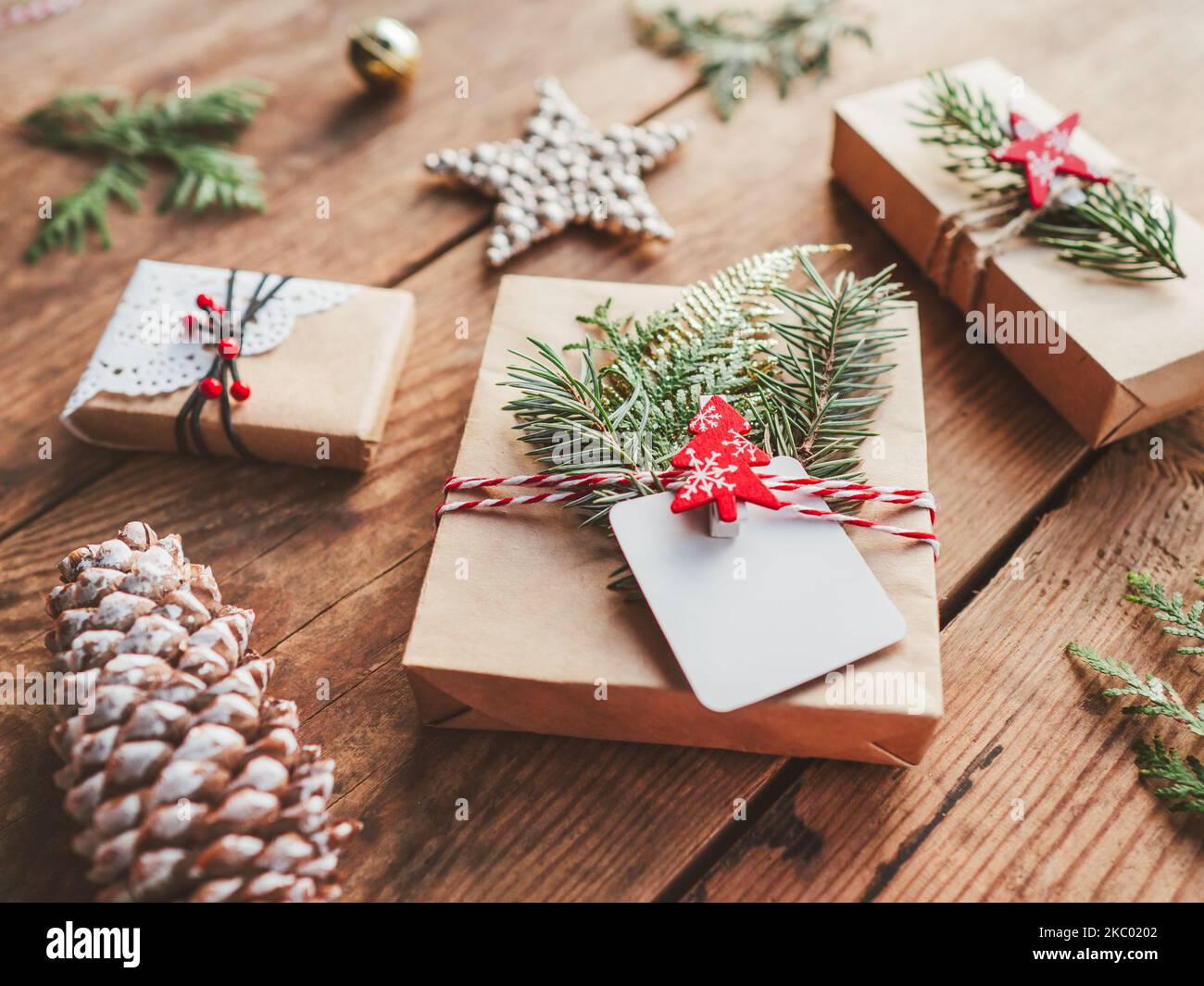 Cadeaux de Noël DIY emballés dans du papier artisanal avec des branches de sapin. Décorations rouges en forme d'arbre de Noël, étoiles. Cadeaux du nouvel an sur table en bois. Banque D'Images