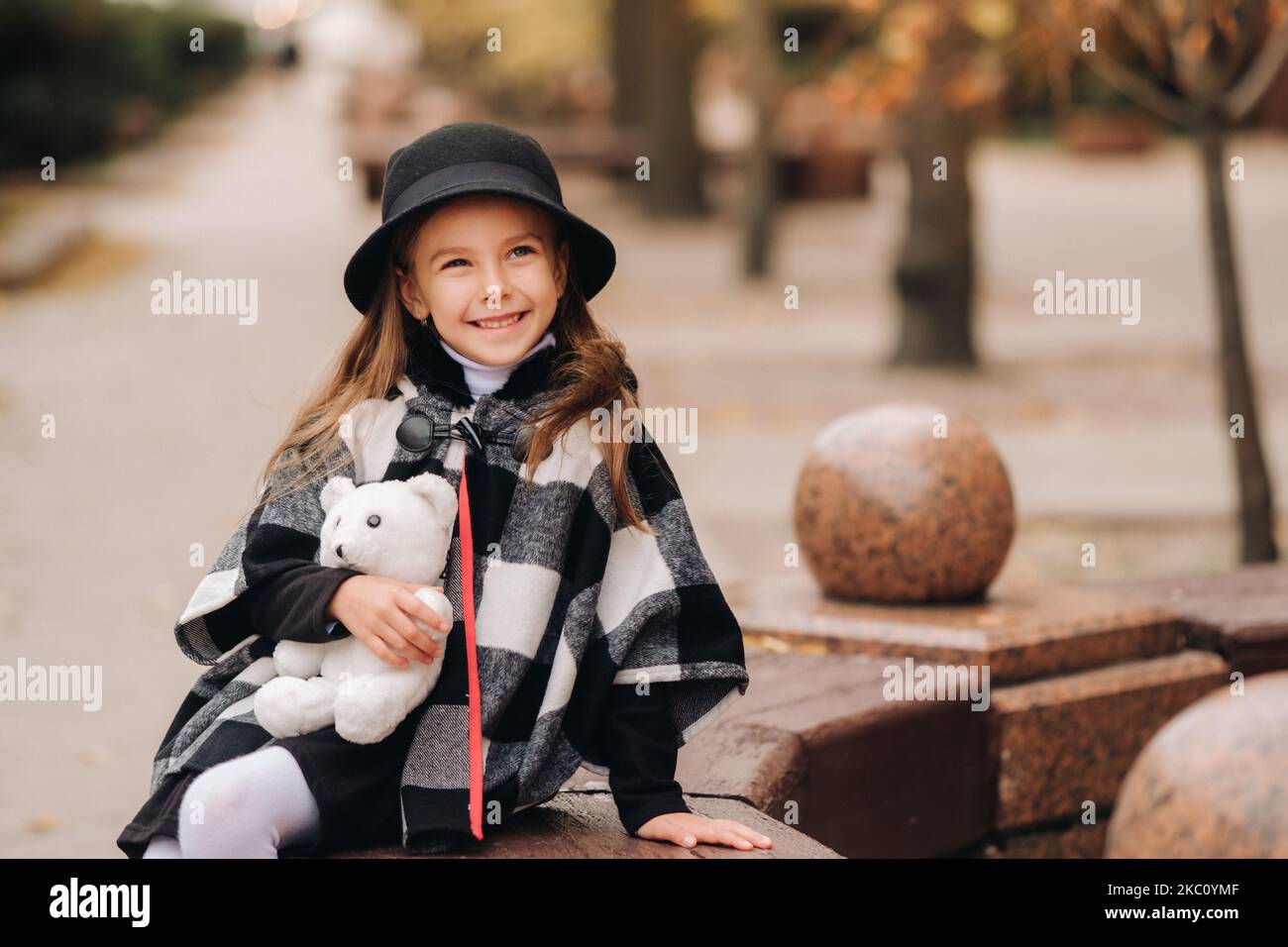 Une petite fille élégante en vêtements d'automne est assise sur un banc dans la ville d'automne Banque D'Images