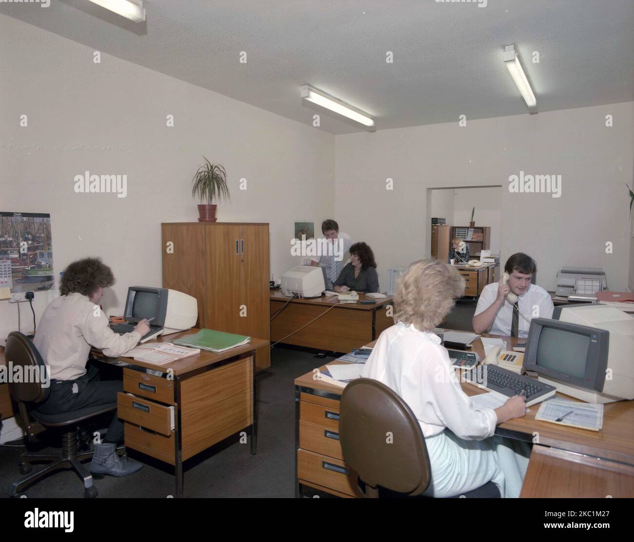 1989, personnel historique, masculin et féminin dans un bureau ouvert, assis à des bureaux en bois, travaillant avec les petits terminaux d'ordinateur de l'époque, Angleterre, Royaume-Uni. Banque D'Images