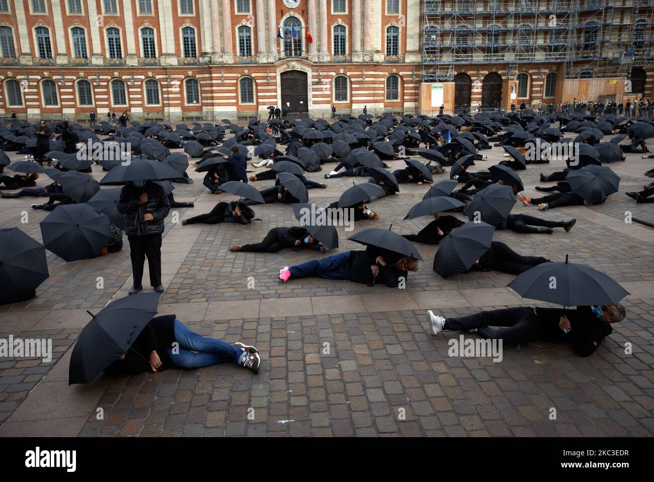 Toutes les personnes se cachent sous un parapluie noir en étant couché sur le sol. Des manifestants, des chefs d'entreprise de divers secteurs économiques (cafés, restaurants, théâtres, librairies...) se sont réunis pour faire un événement contre la fermeture d'entreprises "non essentielles" sur la place principale de Toulouse, le Capitole. Ils ont fait ce qu'ils ont fait lors d'un confinement imposé en 2nd pour tenter de contenir la propagation du coronavirus du COV-SRAS-2 qui cause le caractère inhumain de Covid-19. Ces secteurs sont les plus durement touchés par la crise économique, ils demandent des mesures concrètes de la part du gouvernement. Ils ont utilisé des parasols noirs pour symboliser leur disparition. Banque D'Images