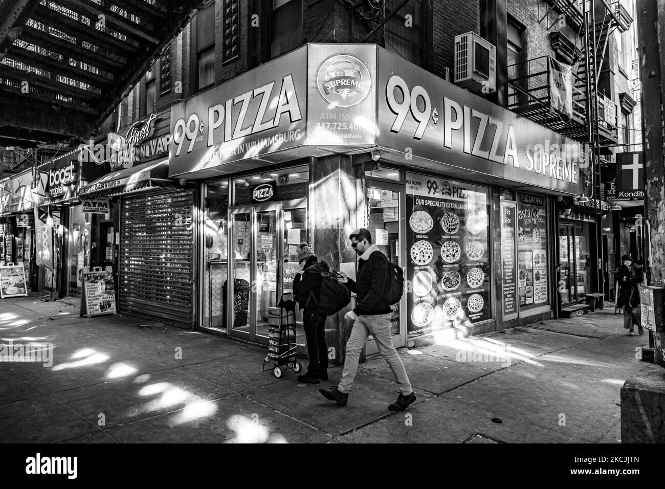 (NOTE DE L'ÉDITEUR: L'image a été convertie en noir et blanc) Un homme marchant. Vue quotidienne de la route et de la rue sous le pont aérien du métro construction métallique des lignes M, J et Z près de la station Marcy Ave, avec des restaurants, des boutiques, la célèbre pizza dollar tranche, la circulation avec des voitures et des camions et avec des trottoirs dans Broadway Street à Brooklyn, New York. Brooklyn est le comté le plus peuplé de l'État de New York et le deuxième plus densément peuplé des États-Unis. Brooklyn, NY, États-Unis, le 13 février 2020. (Photo de Nicolas Economou/NurPhoto) Banque D'Images