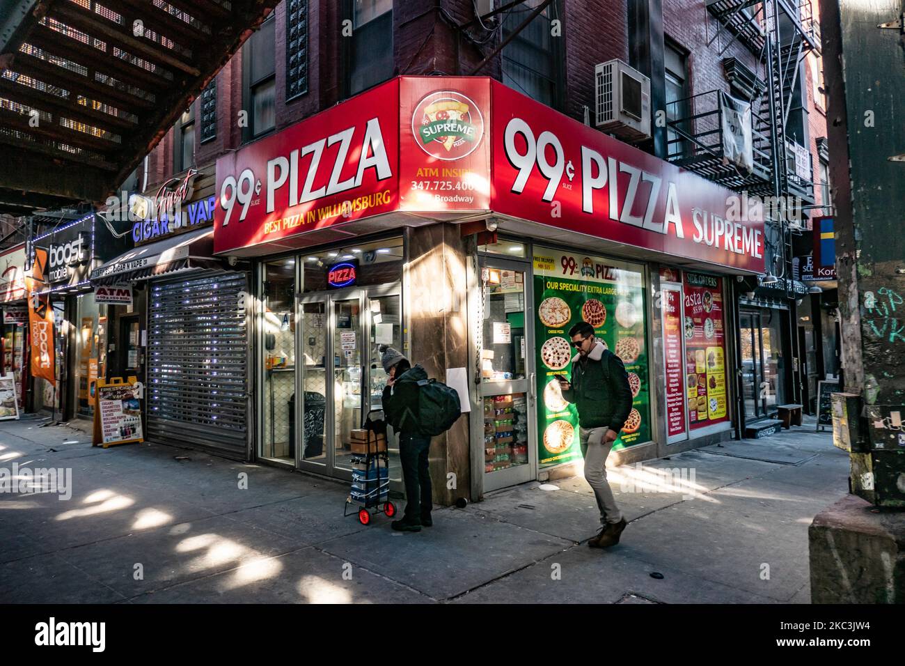 Un homme passant devant une pizza de 99c tranches de dolar tenant son téléphone et marchant. Vue quotidienne de la route et de la rue sous le pont aérien du métro construction métallique des lignes M, J et Z près de la station Marcy Ave, avec des restaurants, des boutiques, la célèbre pizza dollar tranche, la circulation avec des voitures et des camions et avec des trottoirs dans Broadway Street à Brooklyn, New York. Brooklyn est le comté le plus peuplé de l'État de New York et le deuxième plus densément peuplé des États-Unis. Brooklyn, NY, États-Unis, le 13 février 2020. (Photo de Nicolas Economou/NurPhoto) Banque D'Images