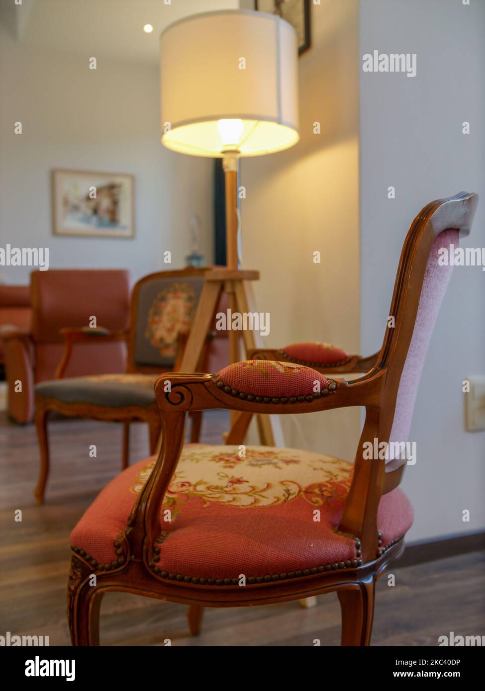 Une photo verticale d'un ancien fauteuil rouge vintage dans une chambre avec parquet et murs blancs Banque D'Images