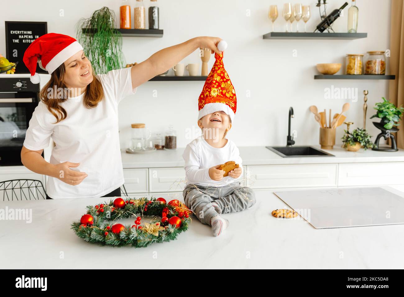 La famille dans de bons esprits pour Noël. Jouer dans la cuisine et se préparer pour les vacances. Maman met un chapeau du nouvel an sur la tête de son fils Banque D'Images