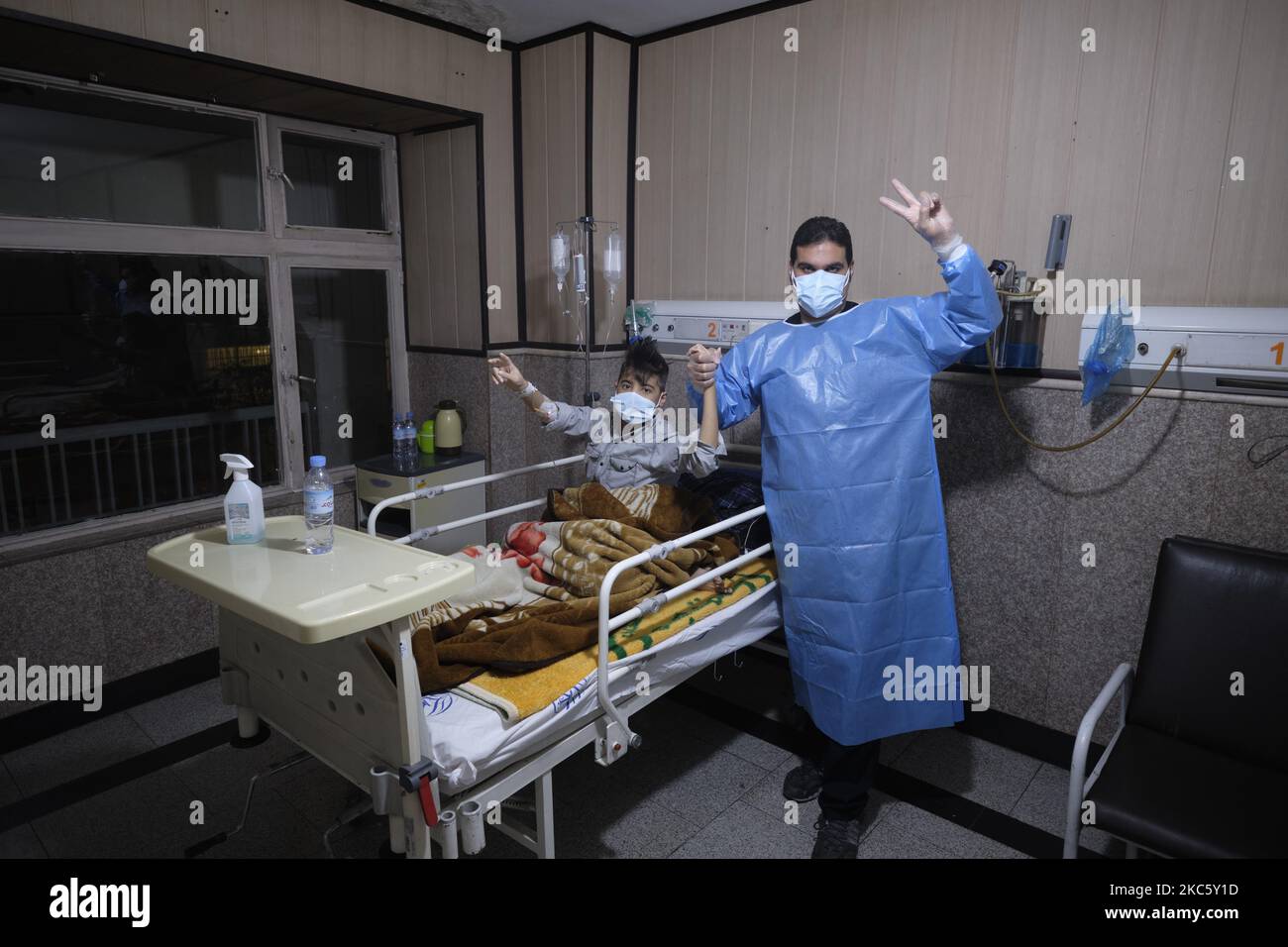 Un personnel médical iranien portant une combinaison protectrice et un garçon de 17 ans qui a été infecté par le nouveau coronavirus, font clignoter le signe de victoire alors qu'ils posent pour une photographie dans une section COVID-19 de l'hôpital Rasoul-e-Akram dans l'ouest de Téhéran la nuit sur 13 décembre 2020. (Photo de Morteza Nikoubazl/NurPhoto) Banque D'Images